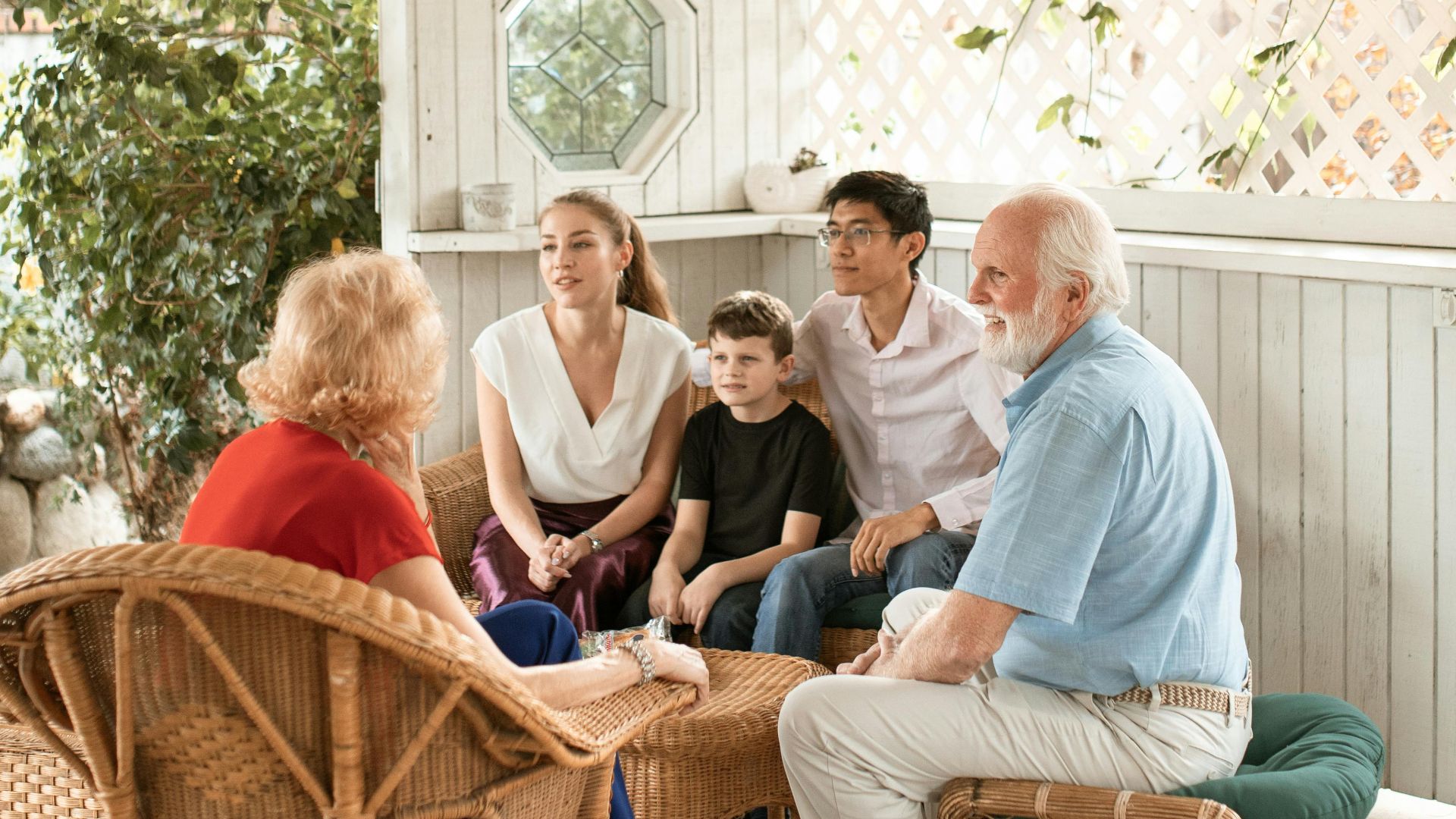 Family enjoys quality time together on cozy outdoor porch with wicker chairs.
