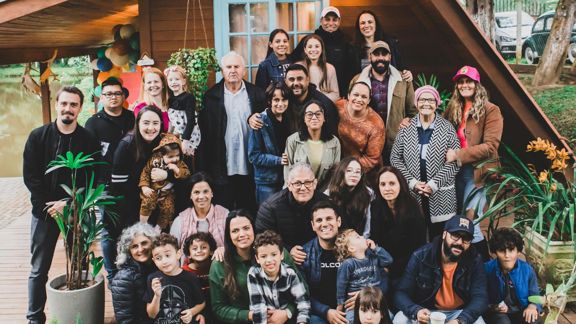 A joyful family group poses together in front of a charming wooden cabin surrounded by nature.