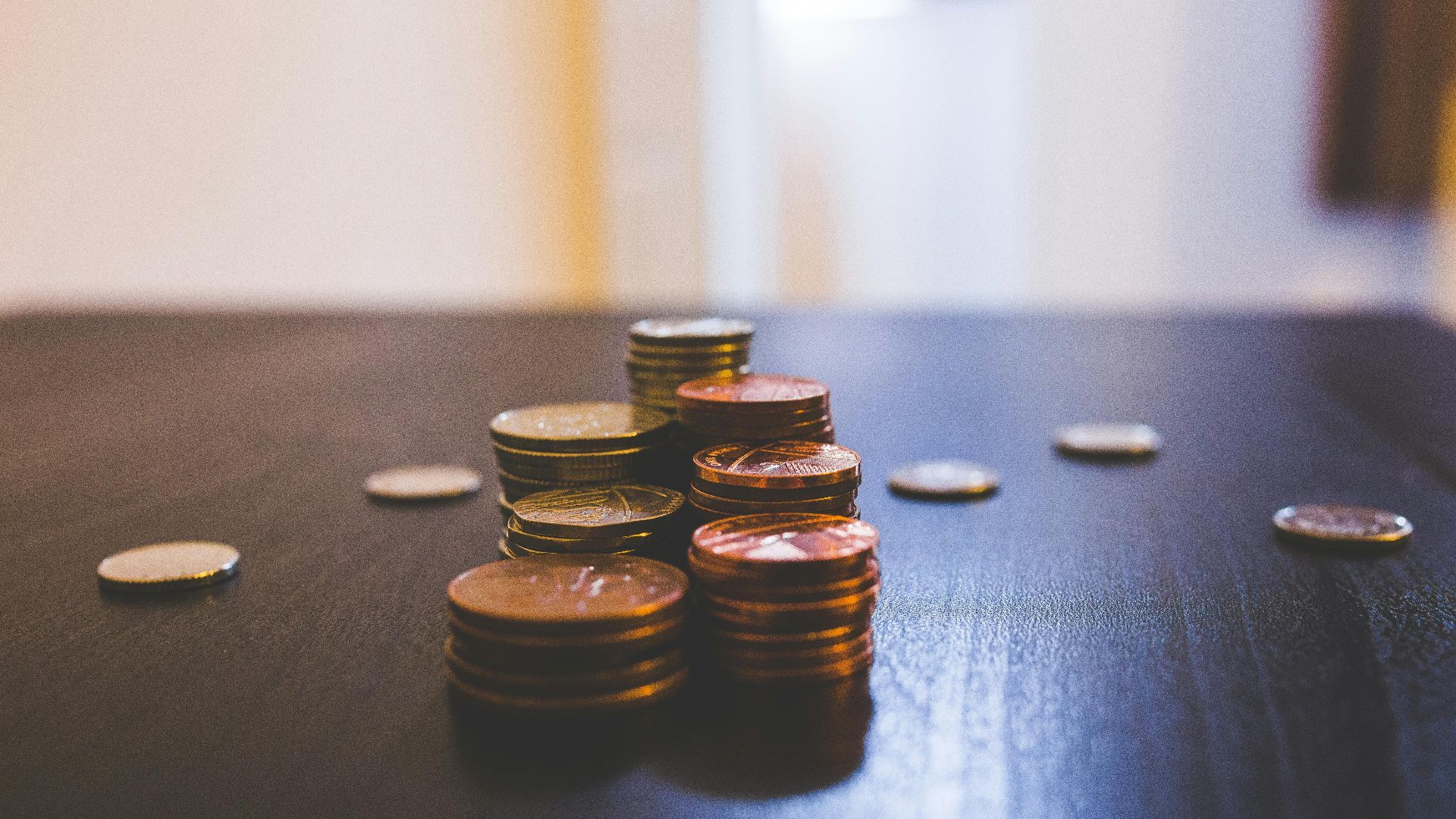 Close-up of various coins stacked on a dark table indoors.