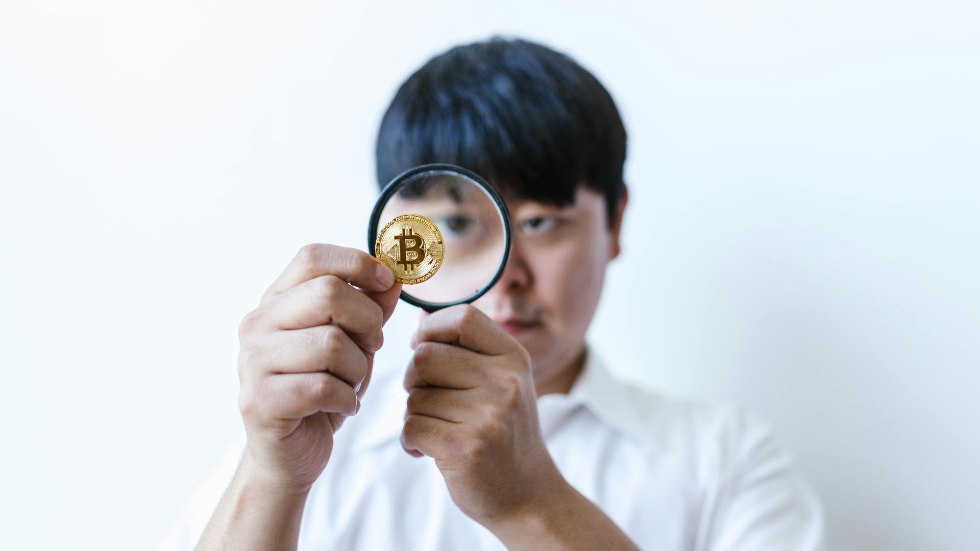 Close-up of a man examining a Bitcoin coin with a magnifying glass, symbolizing cryptocurrency analysis.