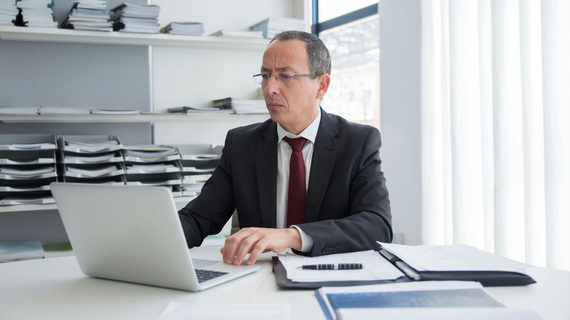Focused businessman in a suit working at his office desk with a laptop and documents.