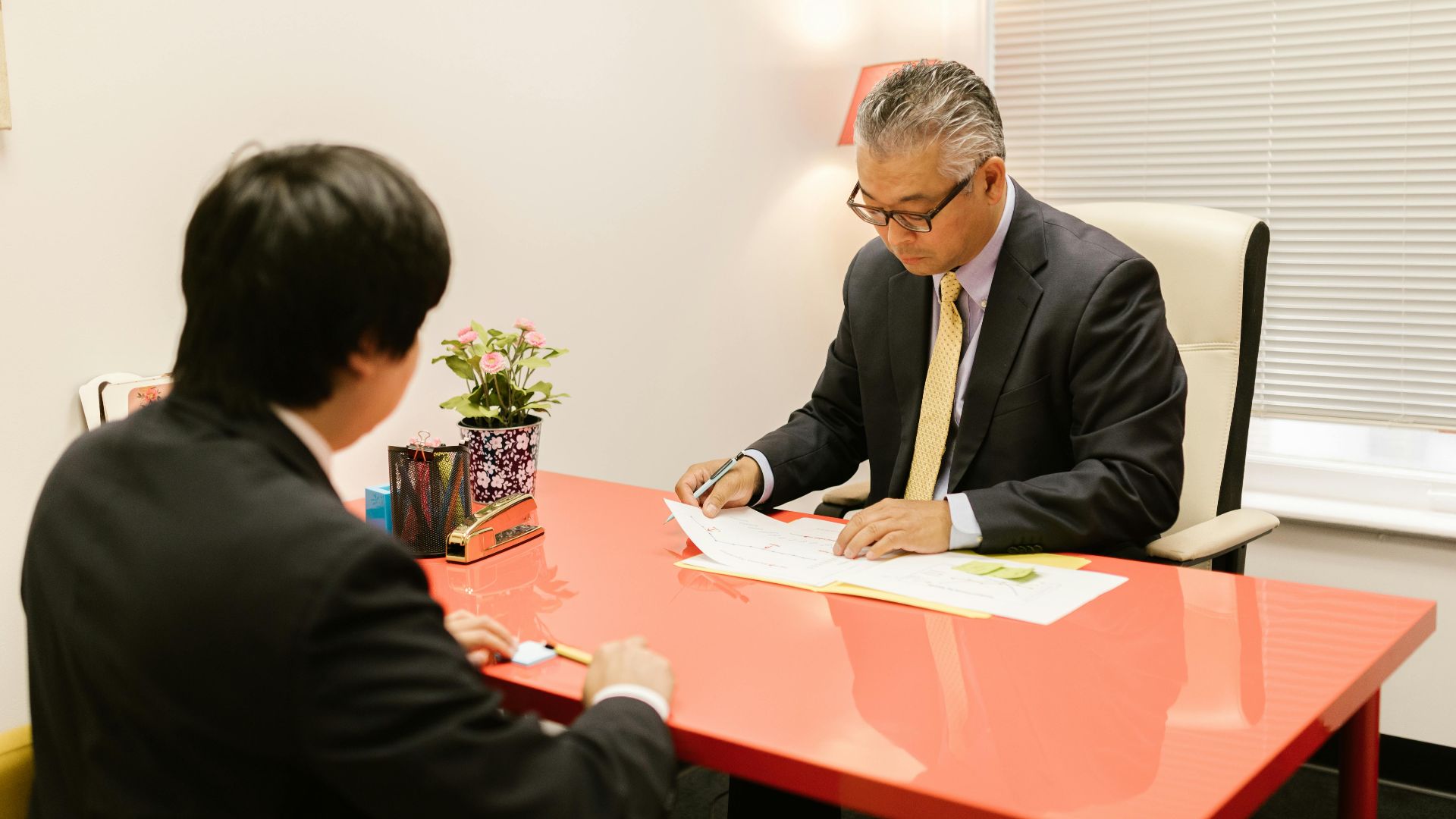 Two professionals discussing documents in a modern office with a red desk.