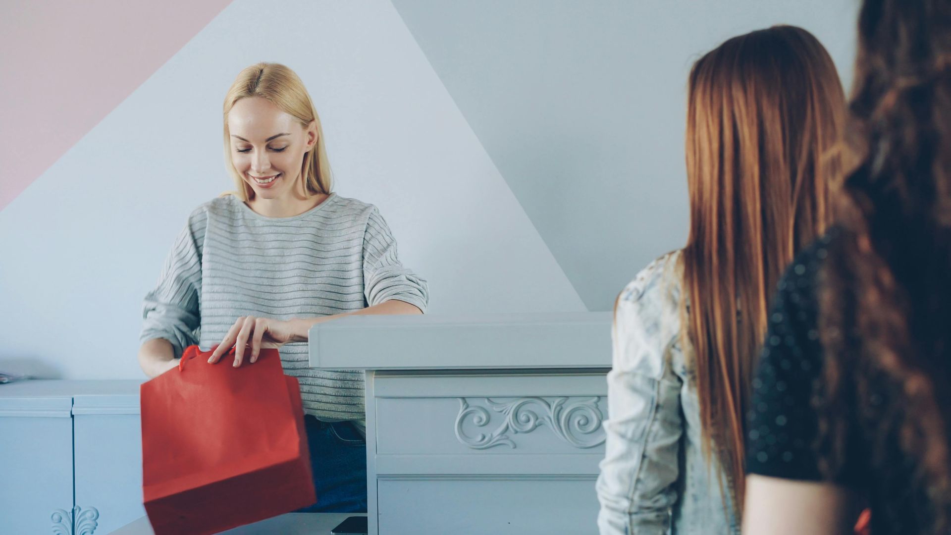 Confident cashier handling a colorful red shopping bag for customers in a vibrant store.