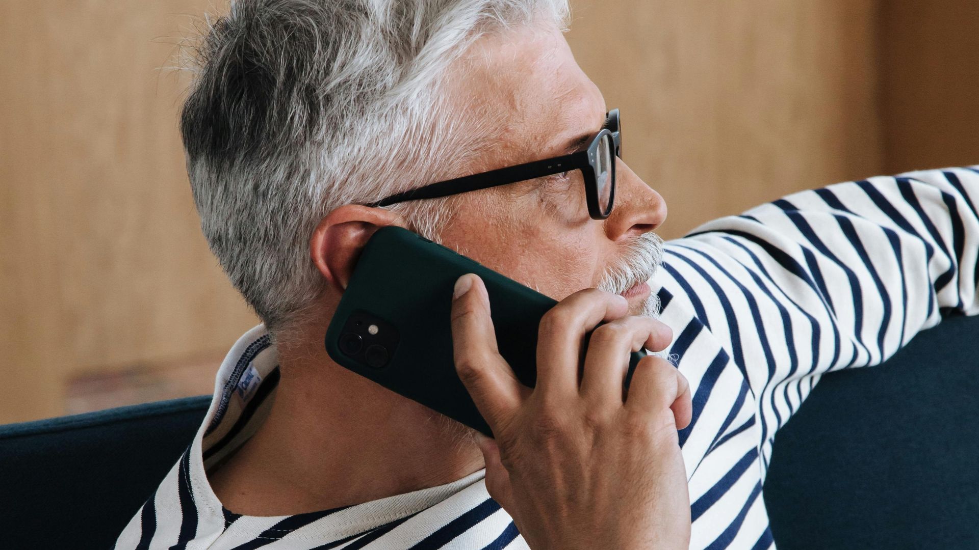 A senior man with grey hair using a smartphone while relaxing at home.