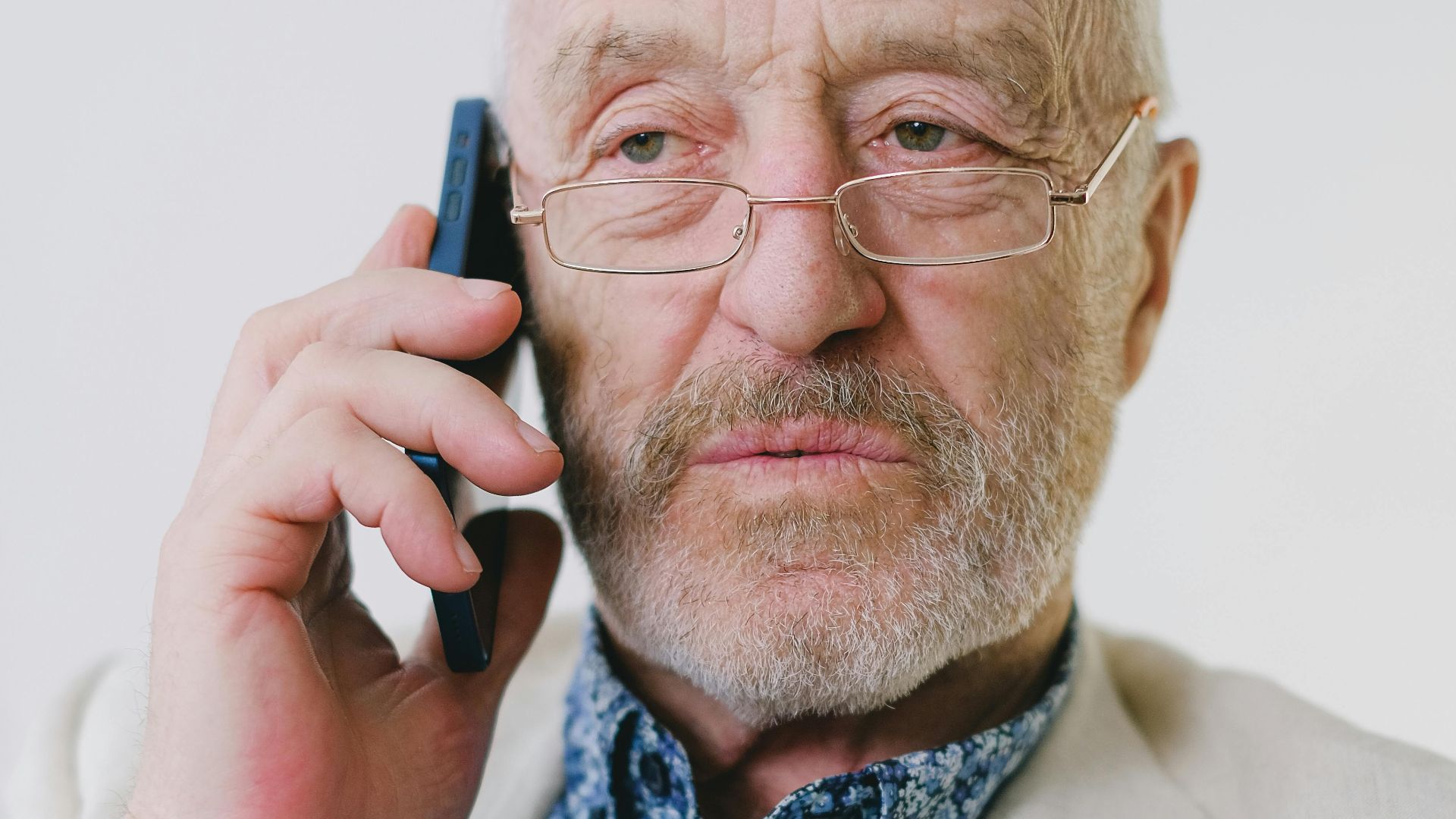 Portrait of a senior Caucasian man with eyeglasses talking on a smartphone indoors.