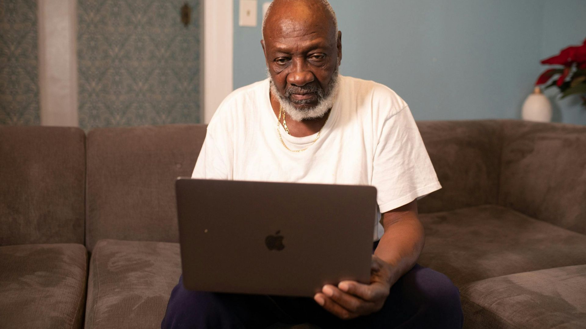 Elderly man sitting on a sofa using a laptop at home, relaxing and focused.