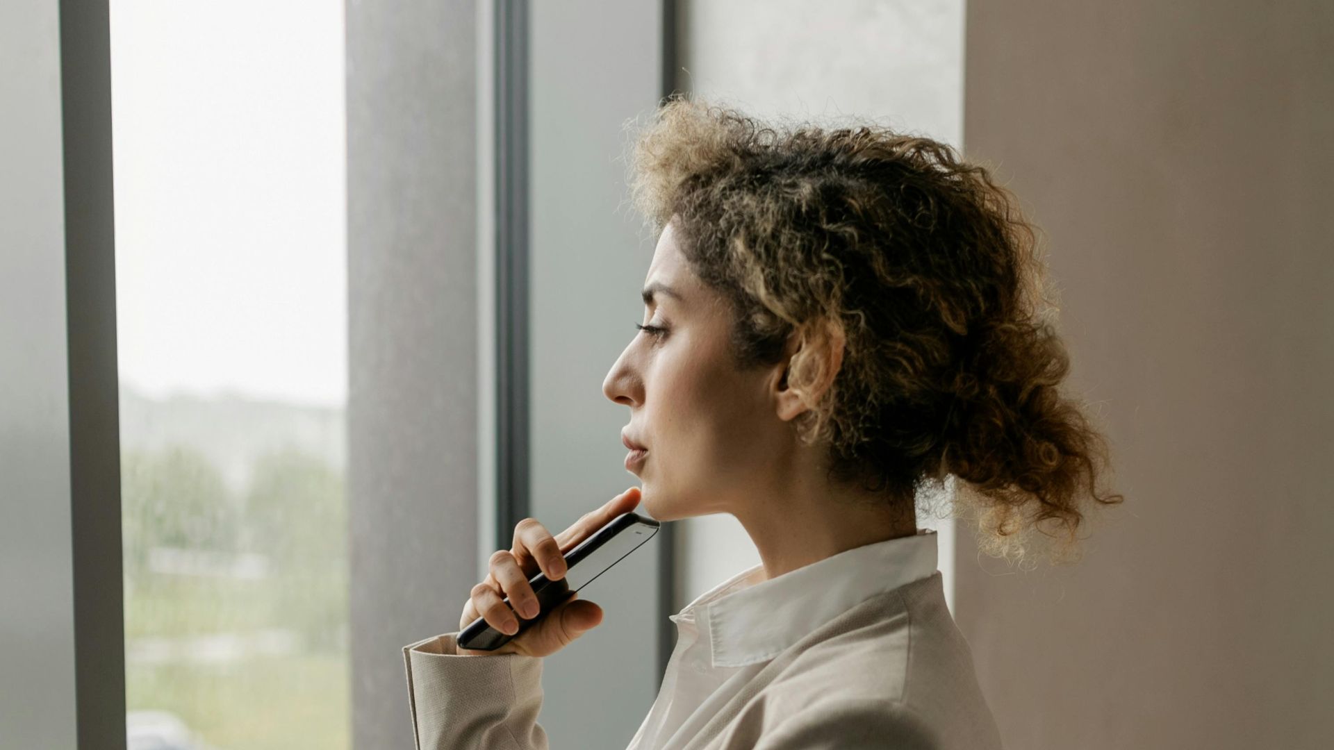 Professional woman in suit looking thoughtfully out a glass window, suggesting corporate environment.