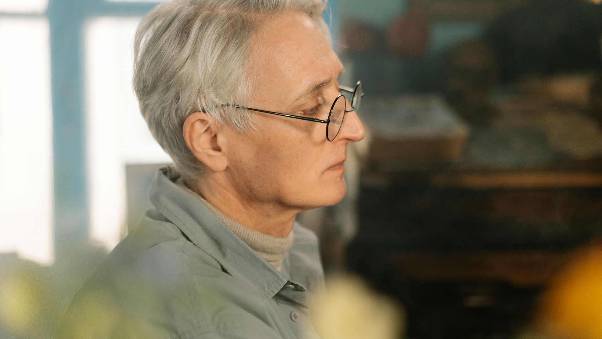 Close-up side profile of a senior man with glasses and gray hair indoors. Warm lighting.