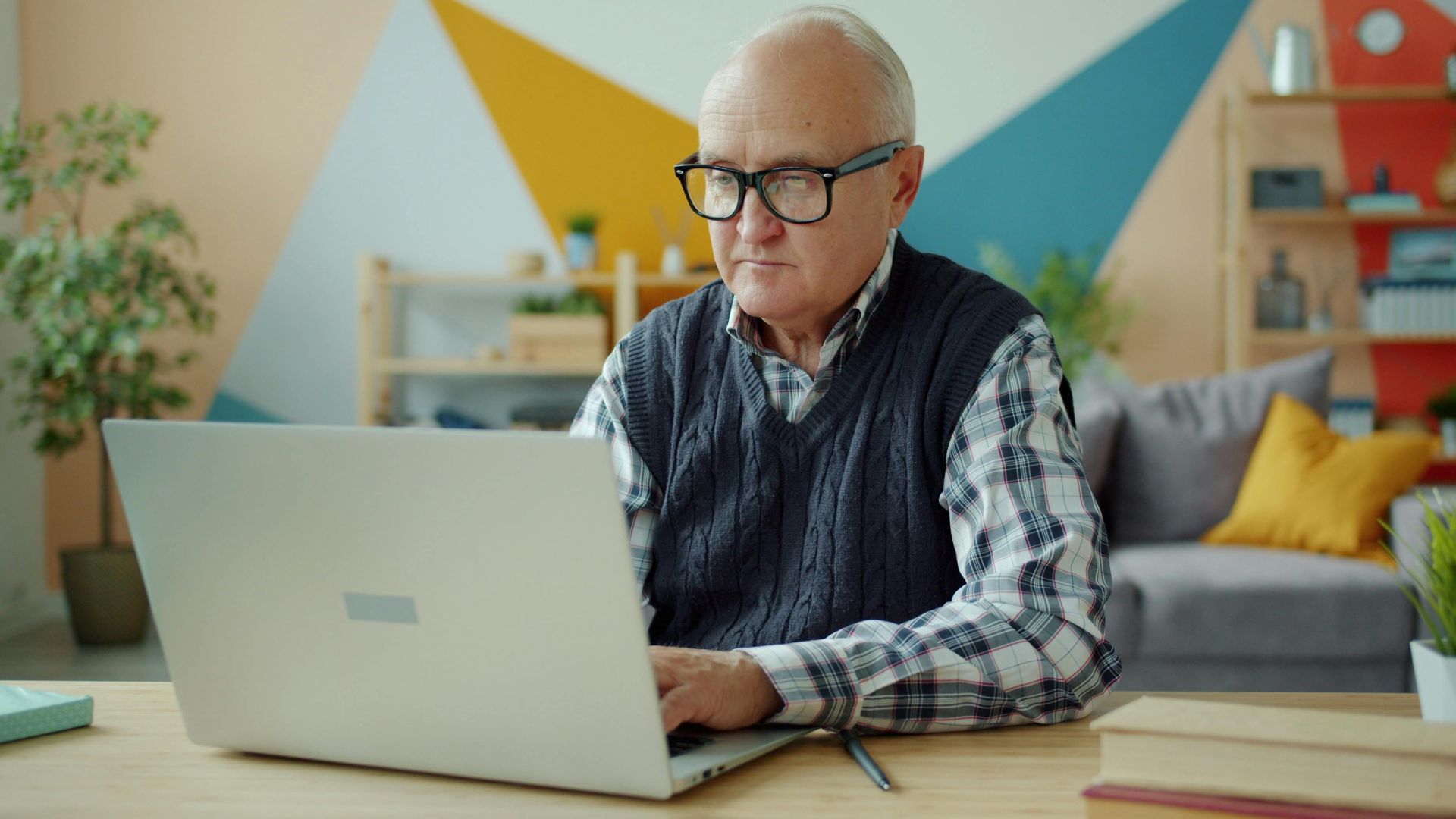 Elderly man using laptop in stylish home office, focused and diligent.