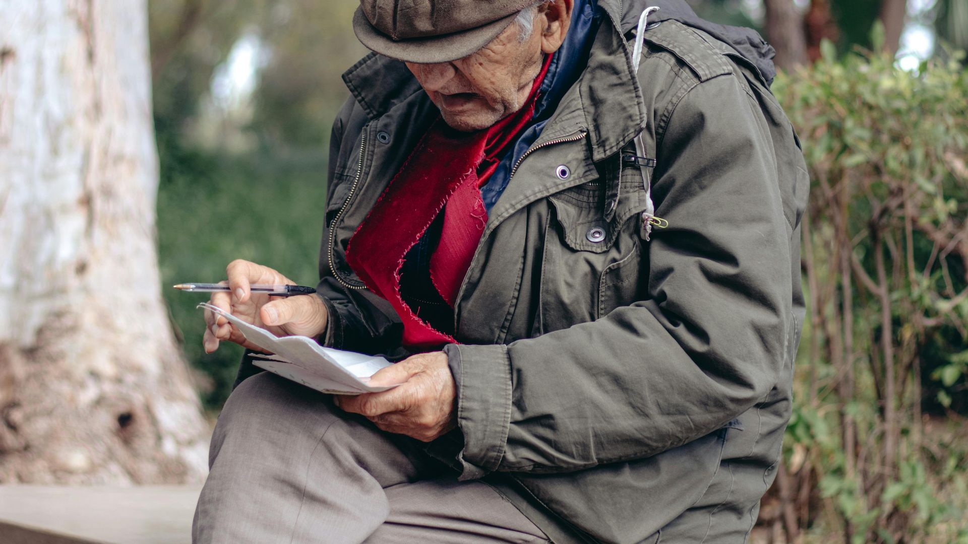 Senior adult writing in a notebook while sitting on a bench in a serene park setting during winter.