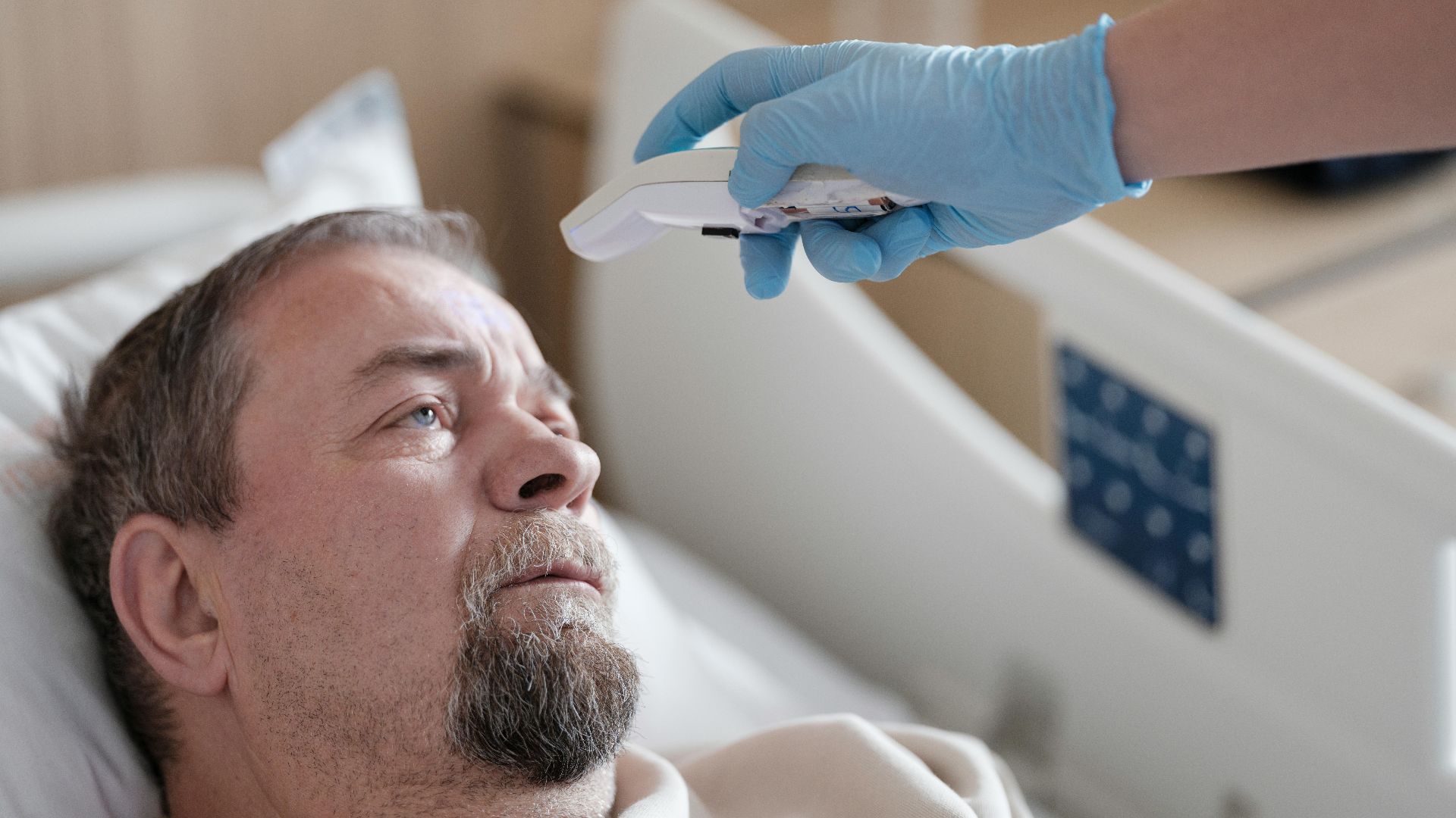 A healthcare professional measures the temperature of a patient using a non-contact thermometer in a hospital setting.