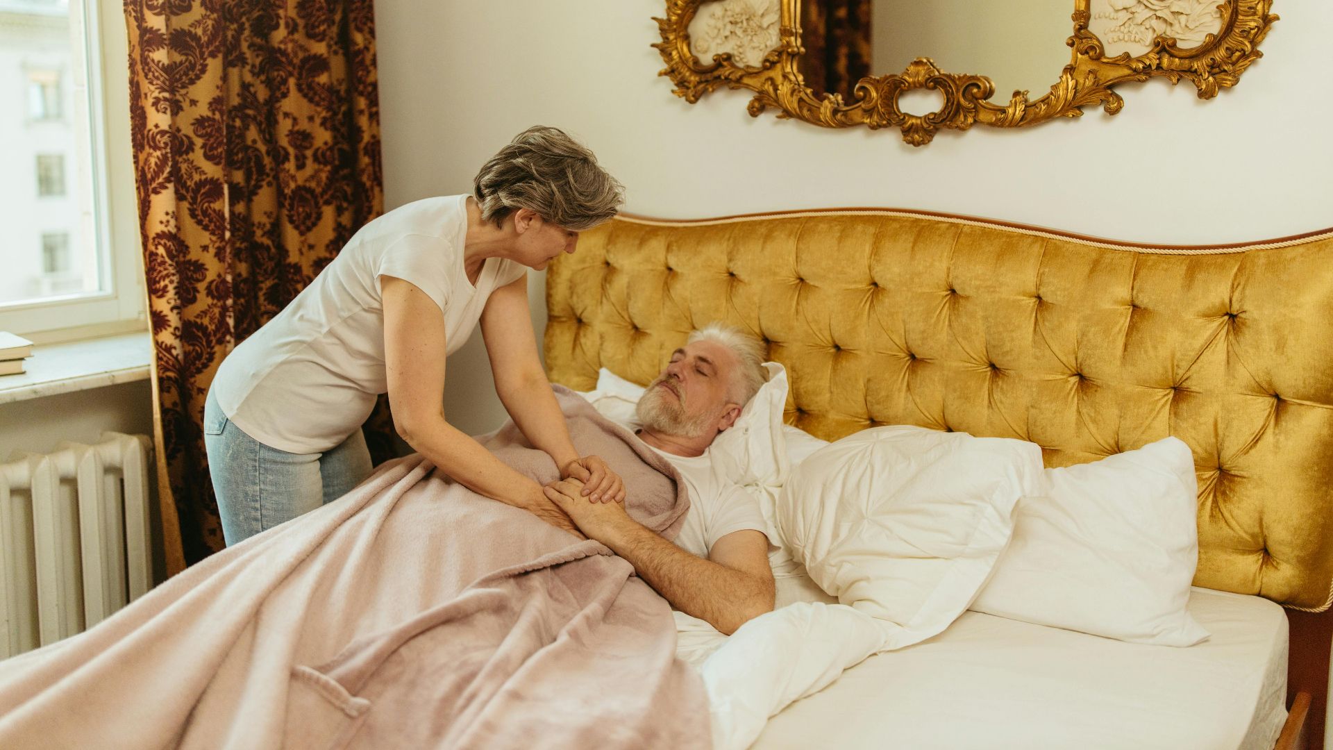 A woman provides comfort to an elderly man lying in bed, showcasing caregiving and family support.