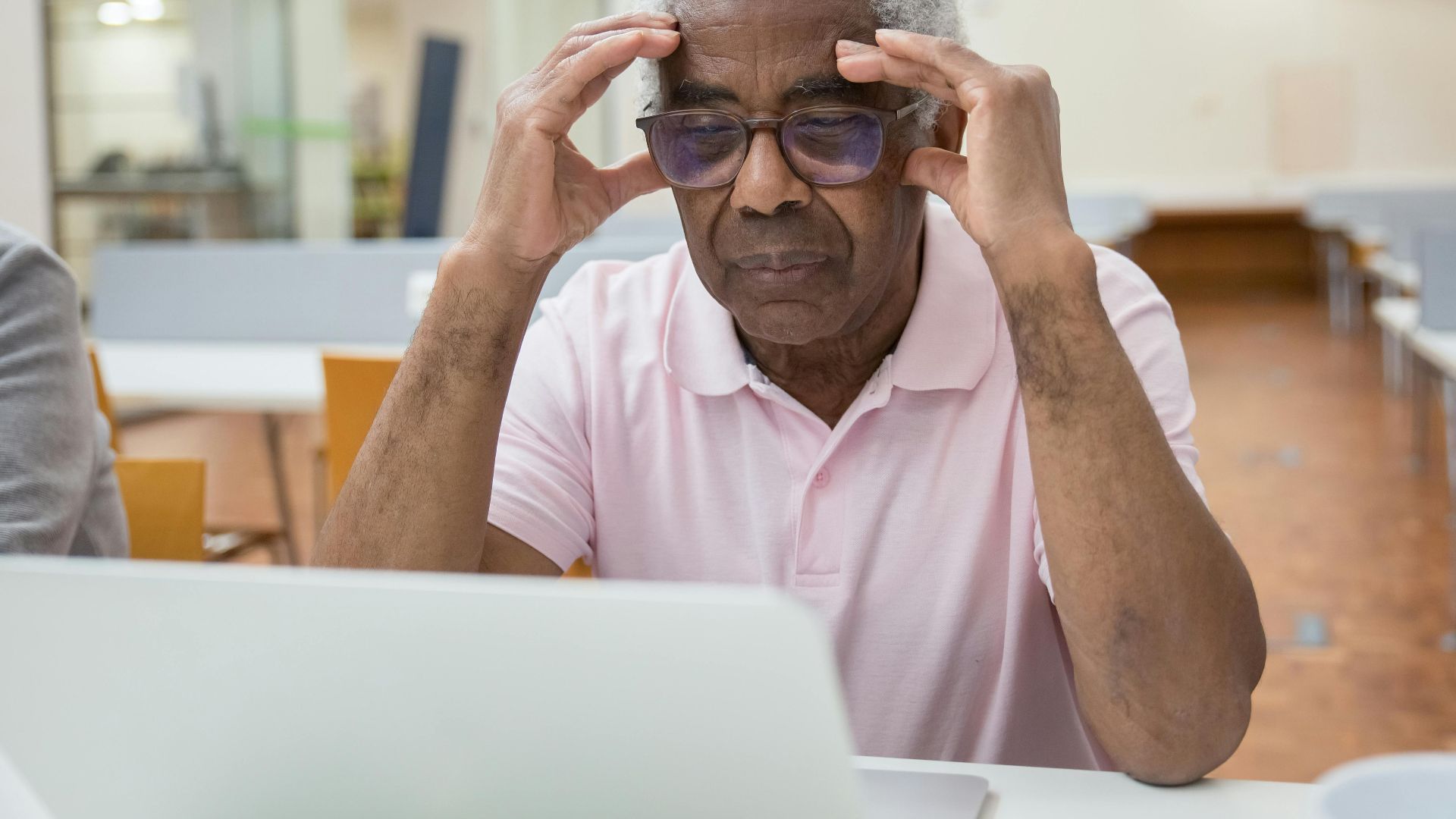 Elderly man deeply focused on laptop work in a modern library setting.