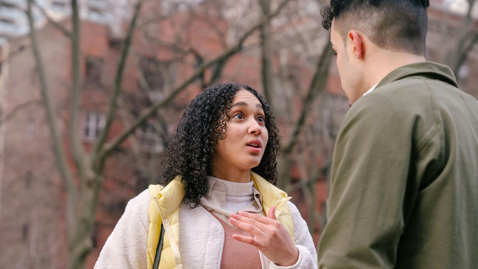 From below of ethnic female with short curly hair standing and arguing with boyfriend on street in daylight