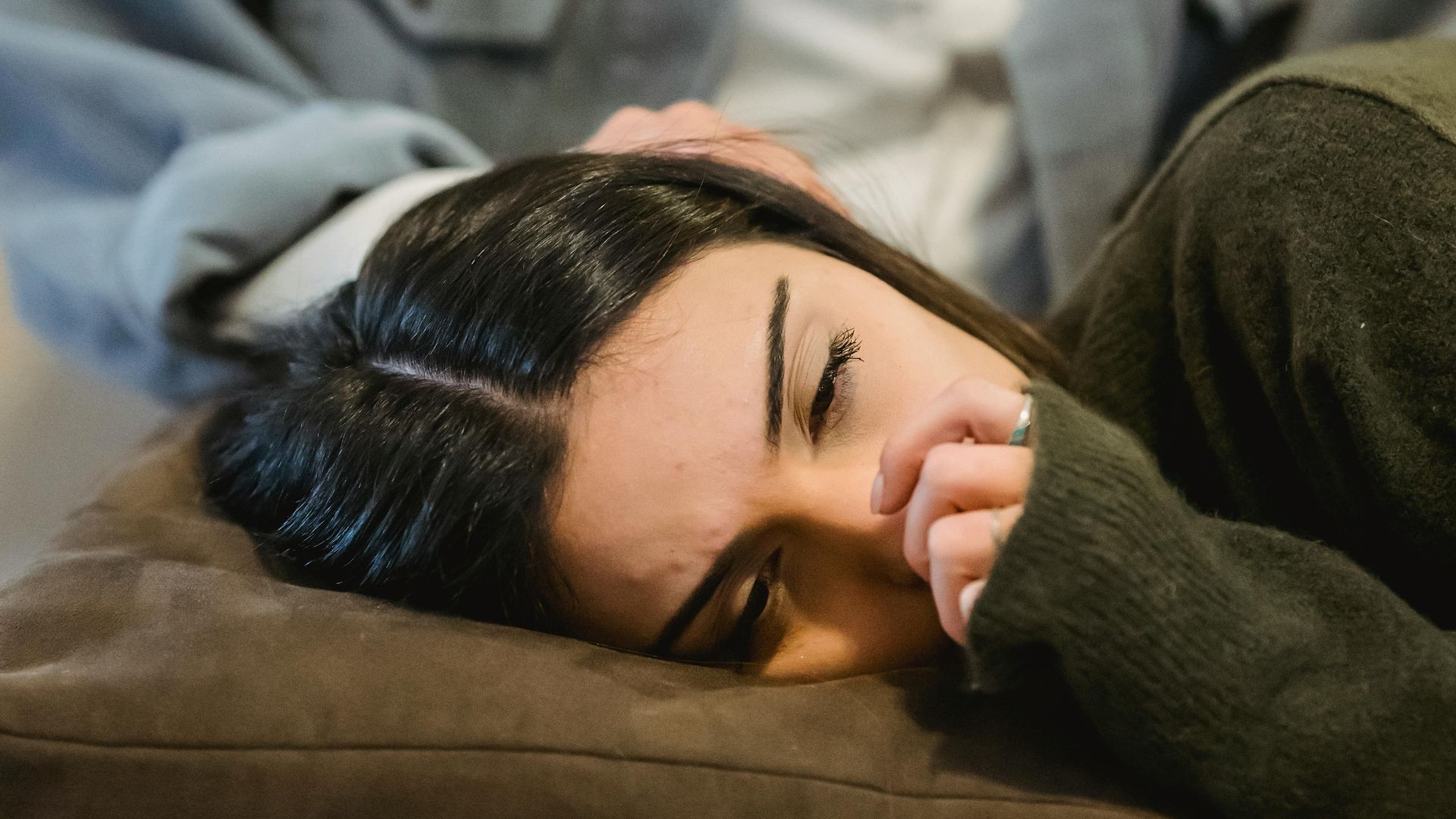 Sorrowful young lady crying while lying on knees of crop ethnic female friend sitting on sofa at home