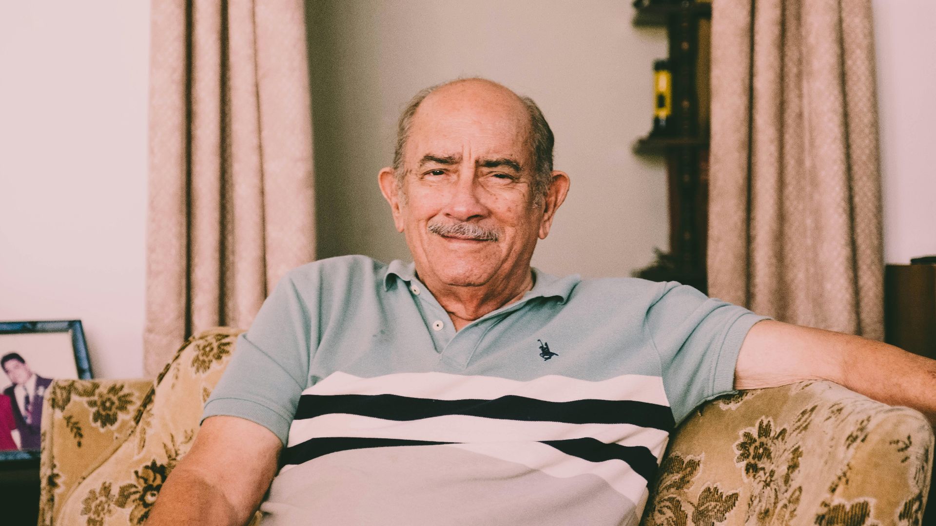 A cheerful elderly man enjoys a relaxed moment on a sofa in a warmly decorated living room.