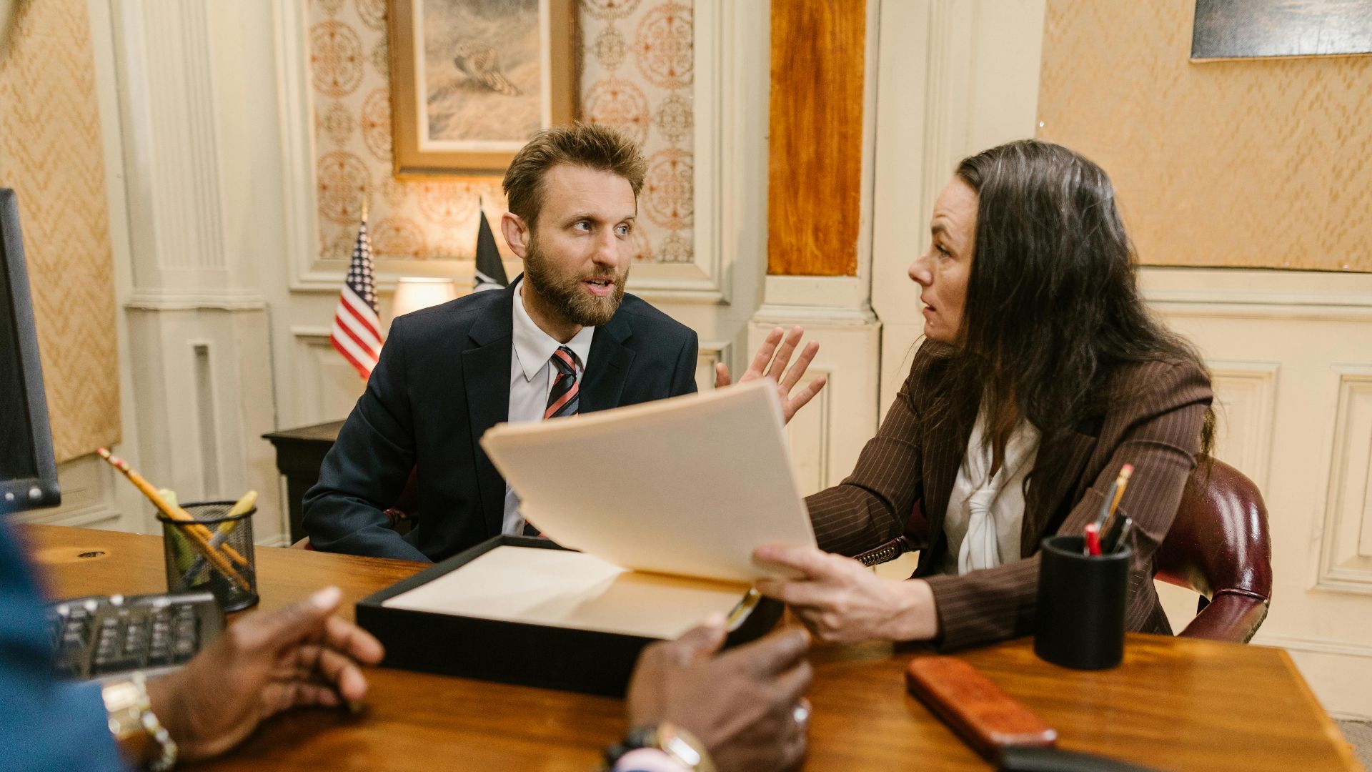 Diverse group in a corporate office engaged in a formal meeting. Professional attire and documents suggest a business discussion.