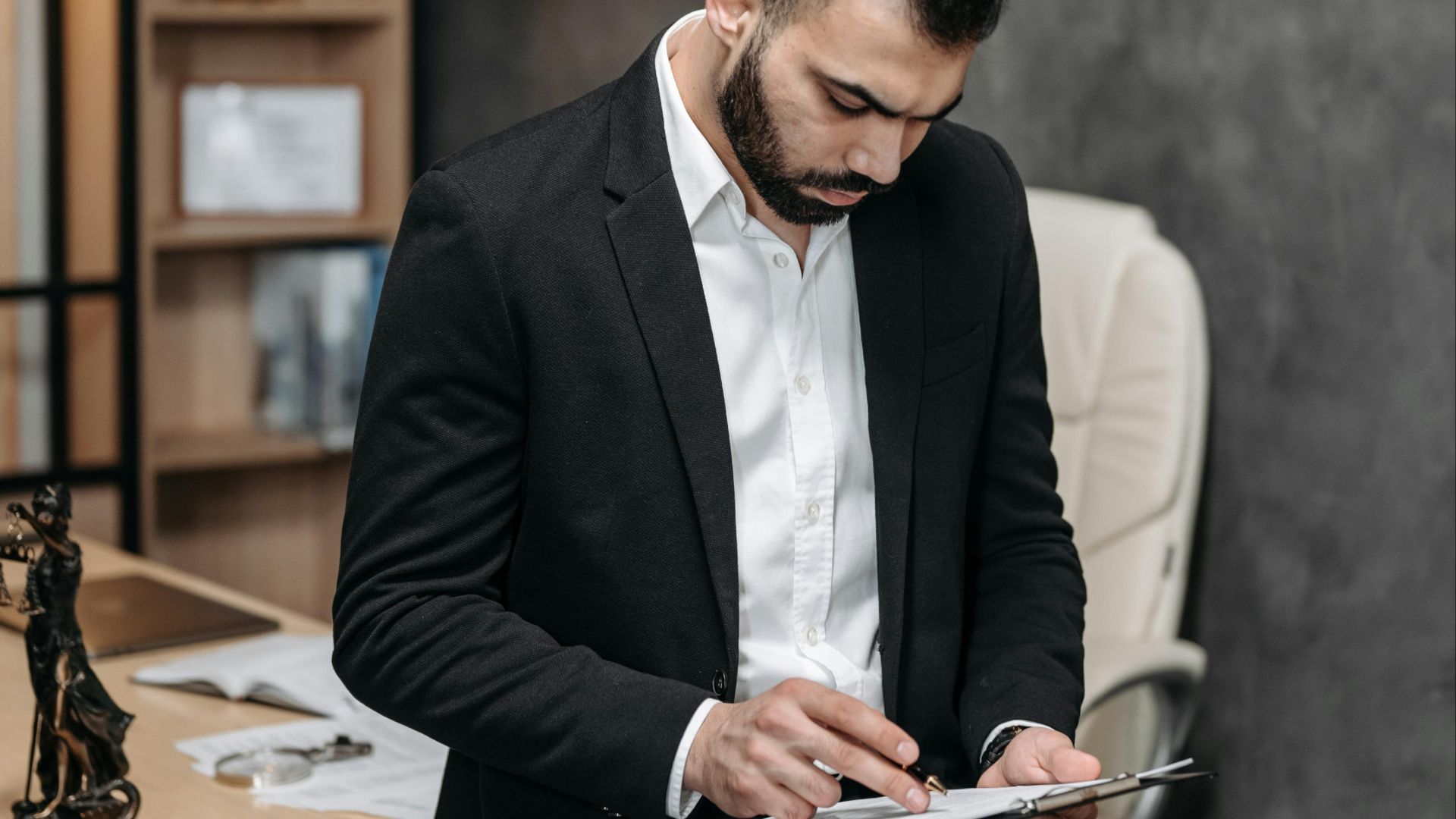 Focused male in suit reviewing paperwork in modern office setting.