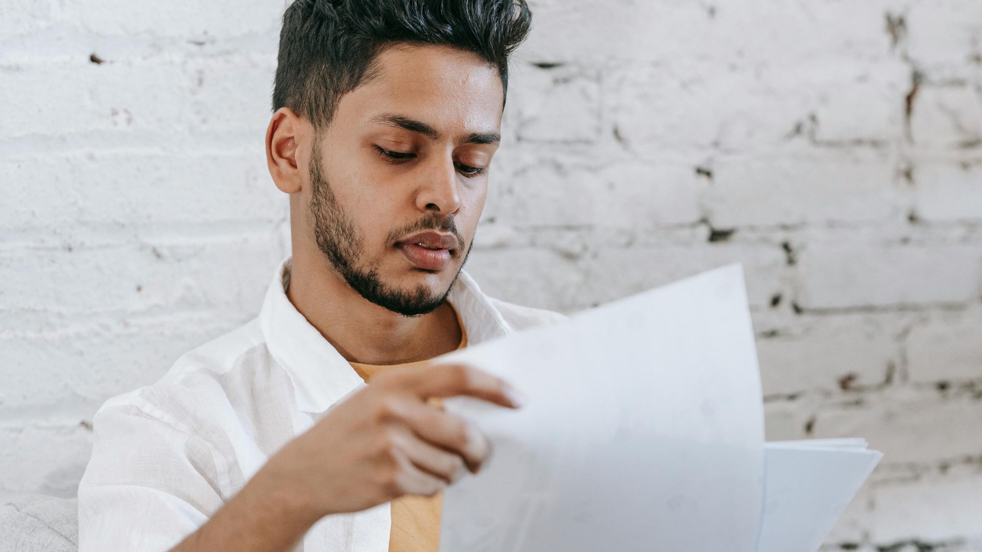 Concentrated young bearded Hispanic male sitting in armchair and analyzing contract while getting job offer