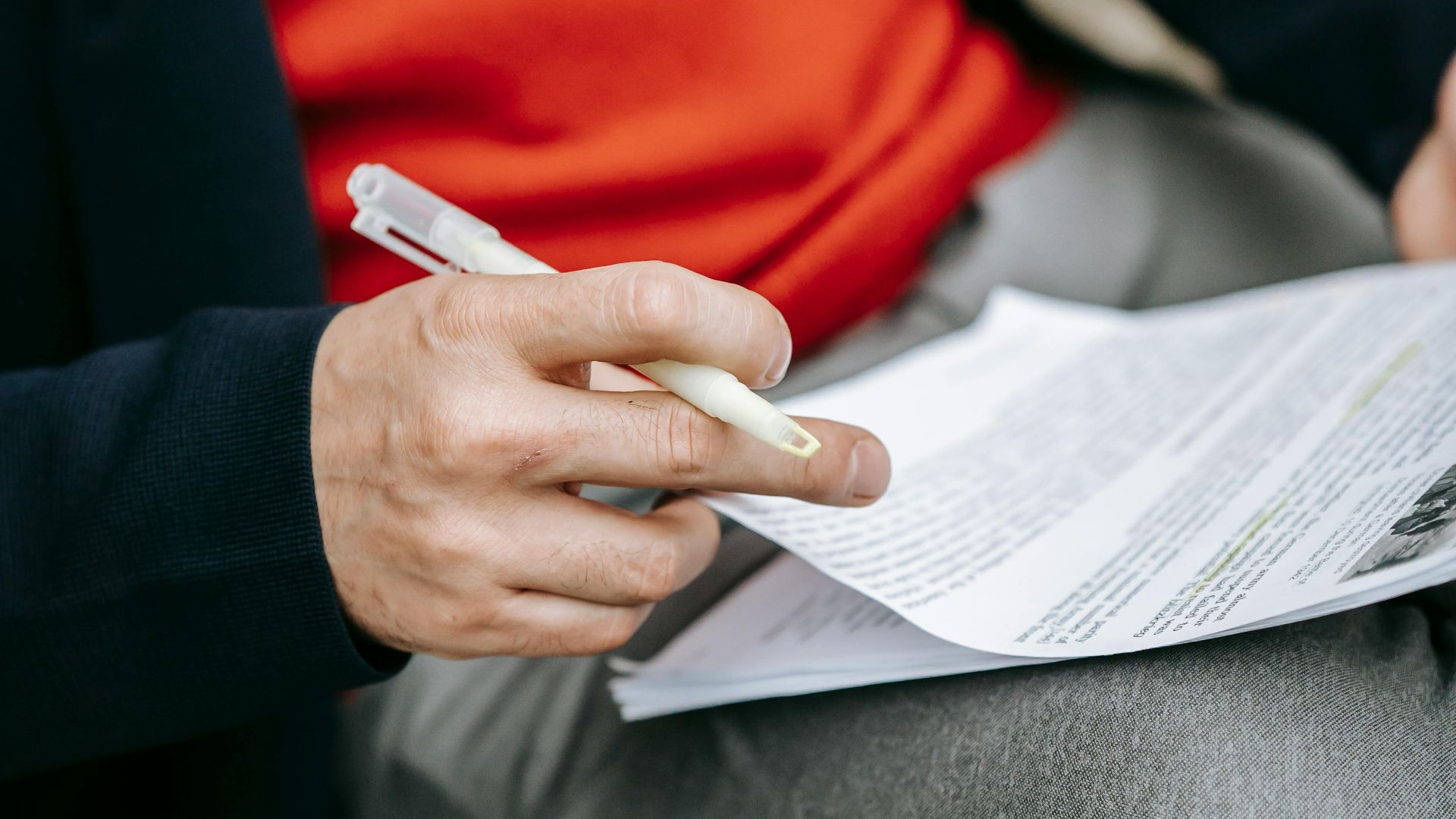 A focused individual reviewing documents outdoors, pen in hand, wearing vibrant clothing.