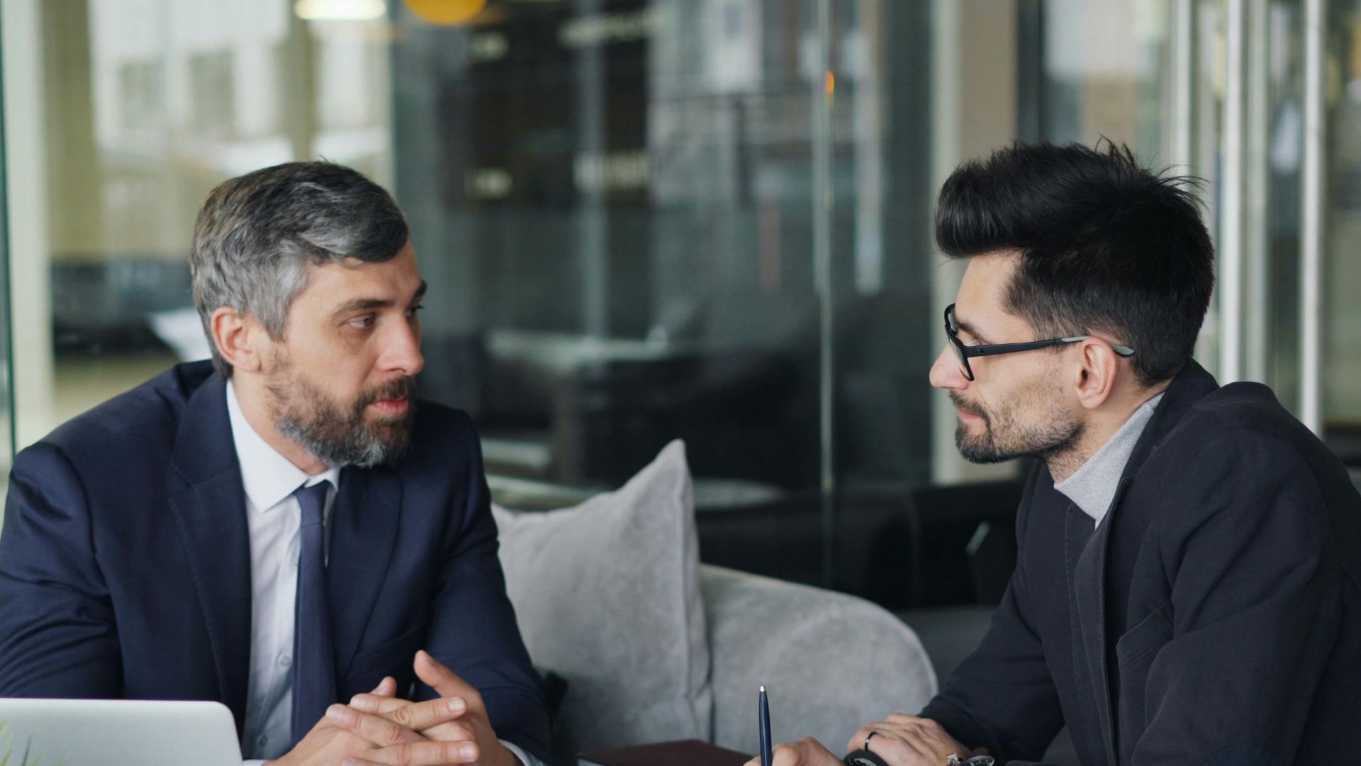 Two businessmen having a meeting with laptops, papers, and coffee at a modern office.