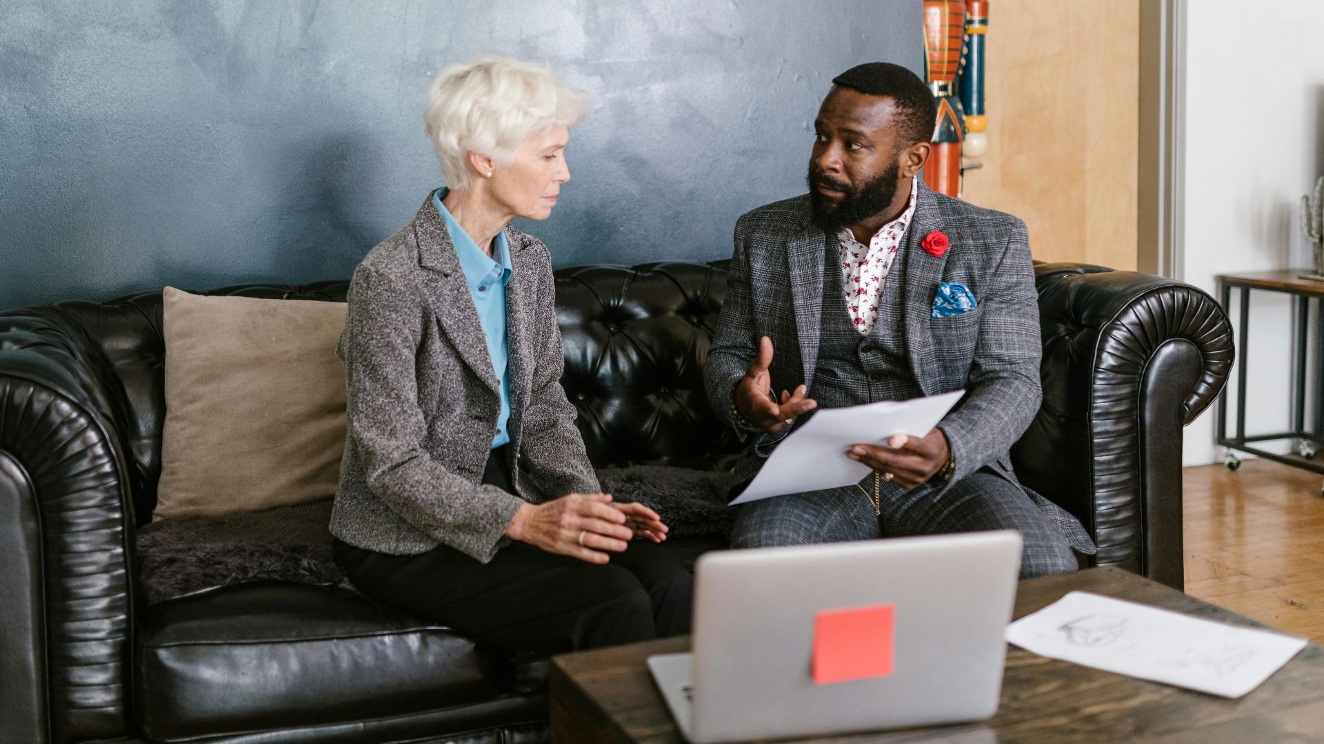 Two professionals engaged in a productive business discussion, seated on a leather couch in an office environment.