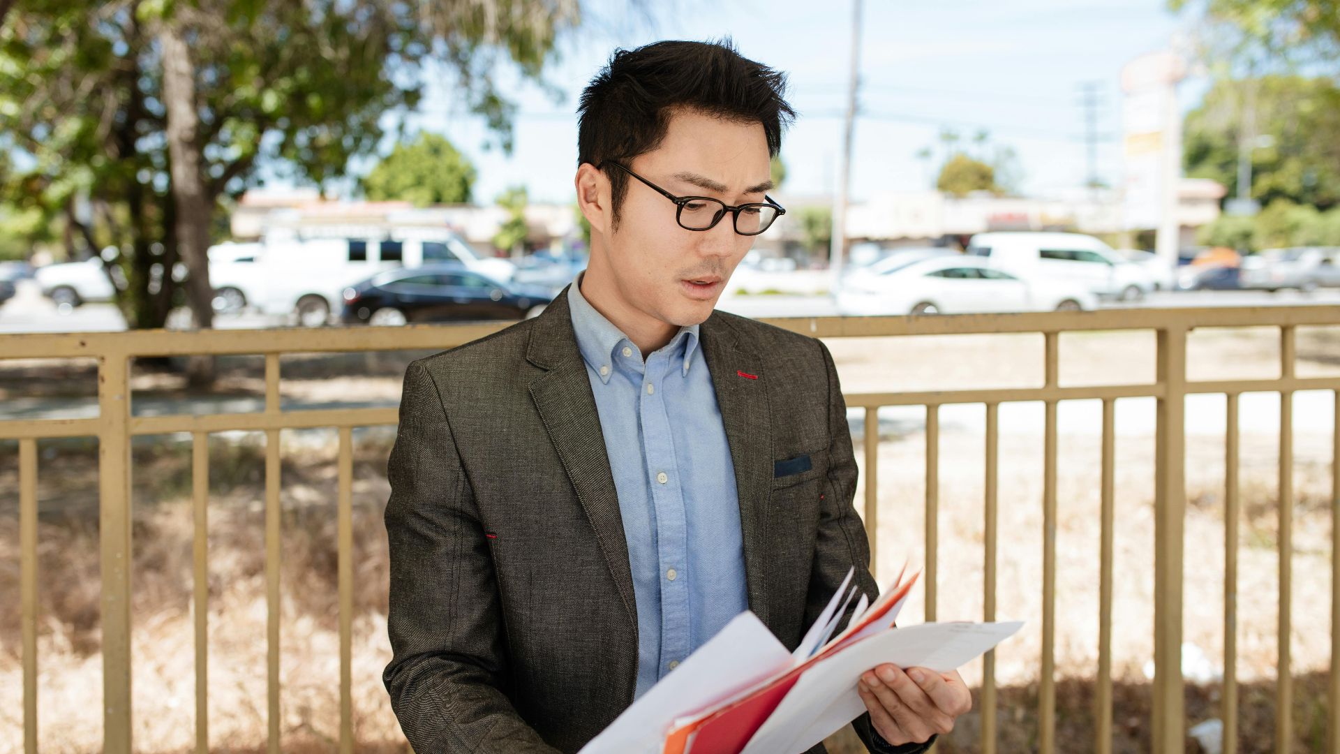 Asian businessman in a suit checking documents outdoors on a sunny day.