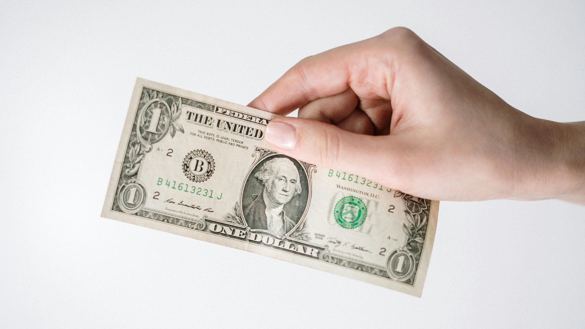 Close-up of a Caucasian hand holding a US one dollar bill against a white background.