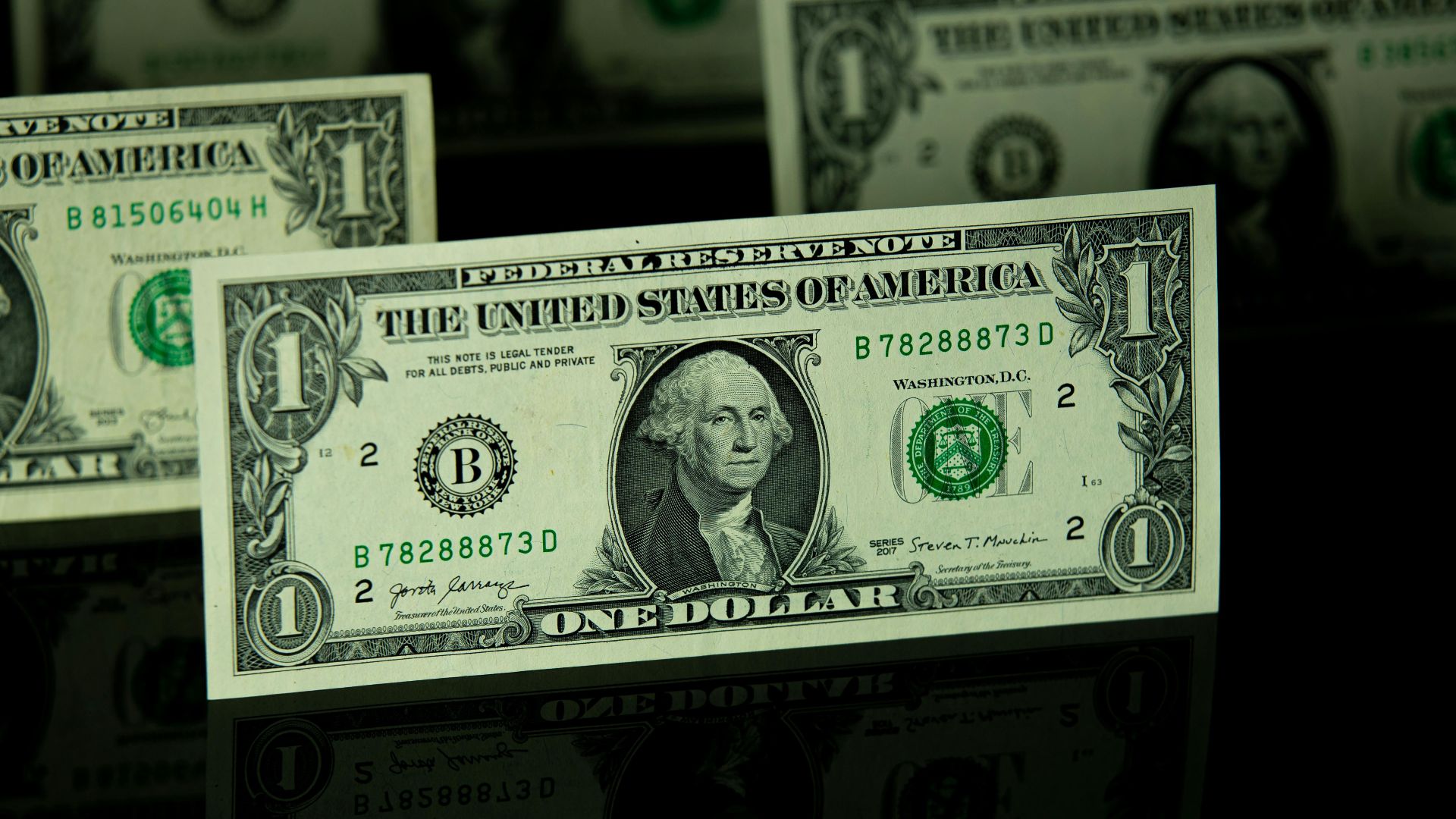 Focused view of US one dollar bills on a reflective black surface.