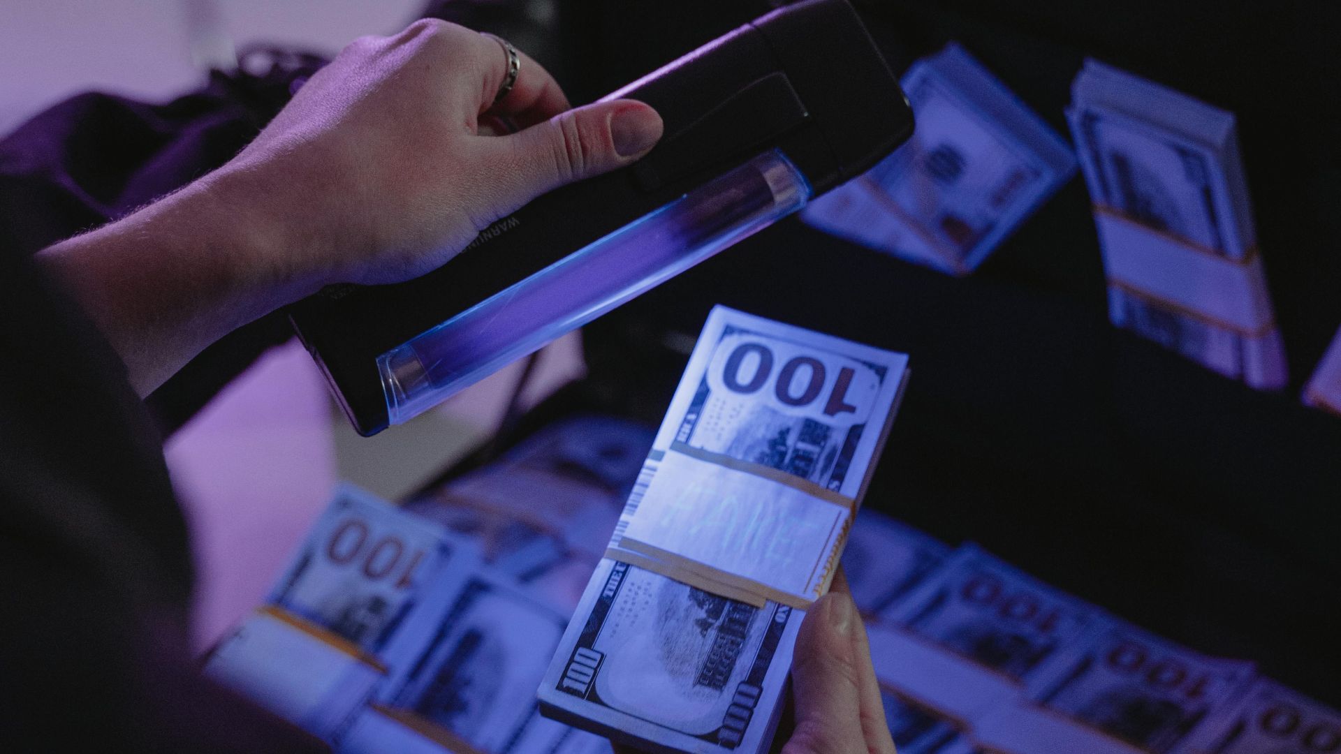 A person examining hundred dollar bills under UV light in a briefcase, ensuring authenticity.