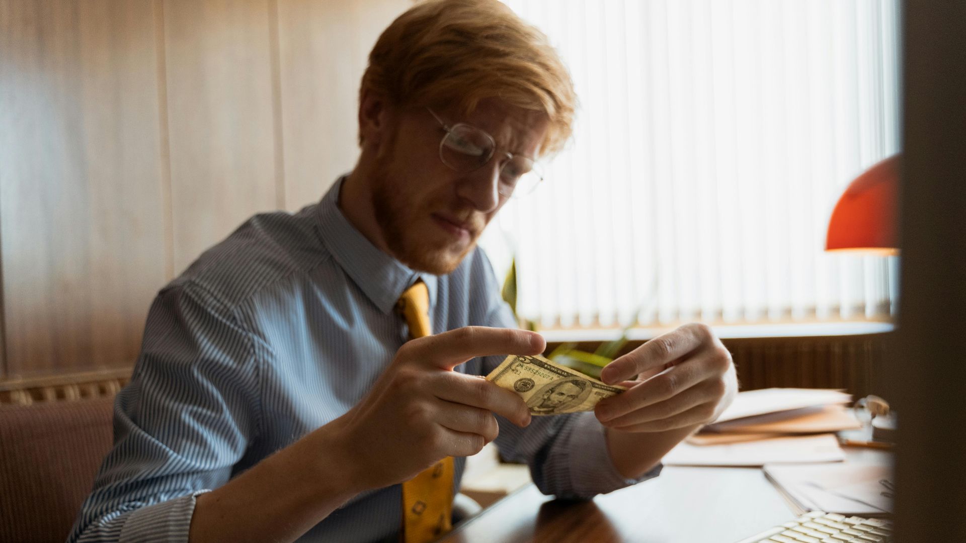 Male entrepreneur intensely examines money at his office desk, representing finance.