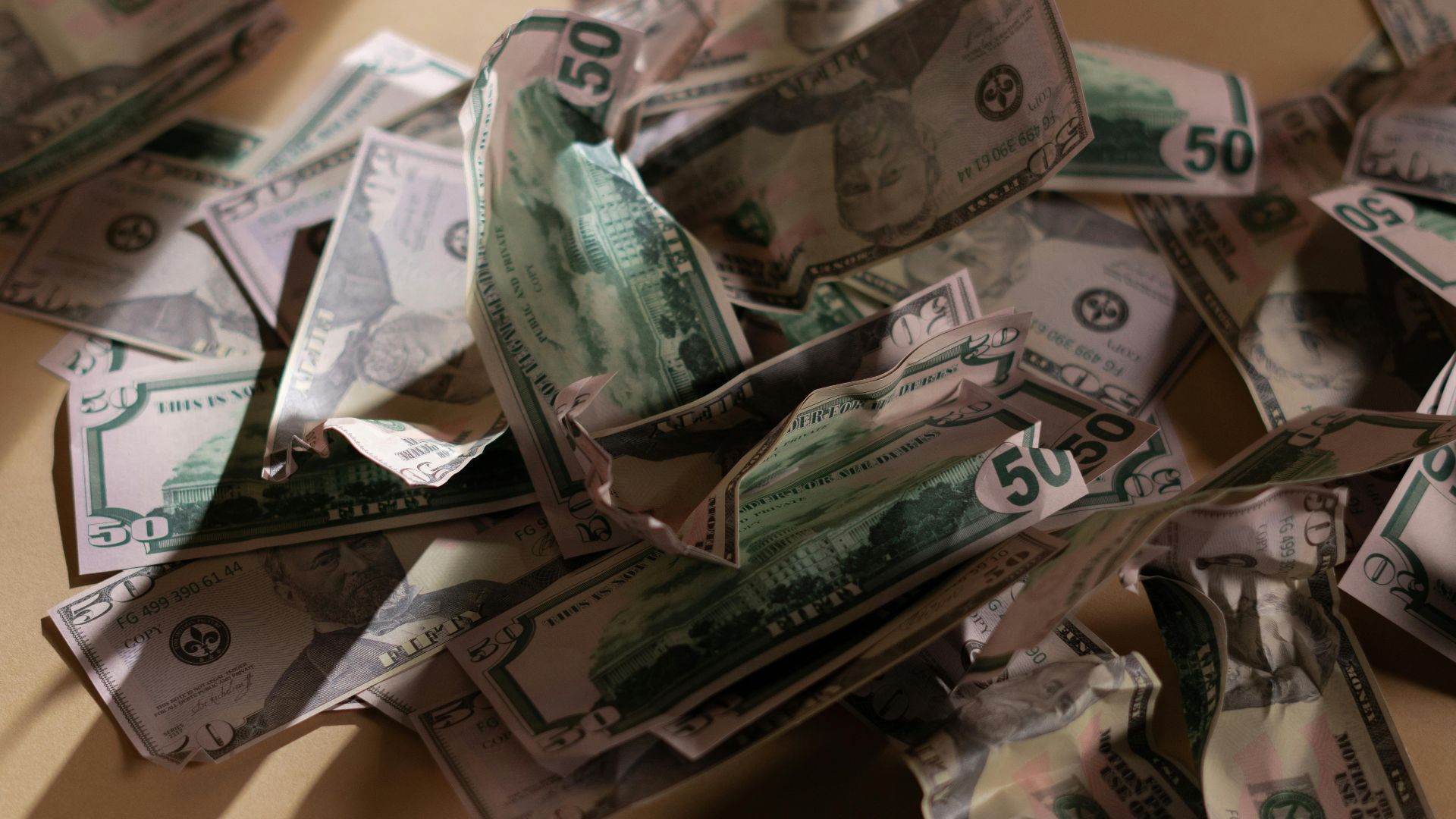 A collection of crumpled US dollar bills spread across a beige surface with natural lighting.