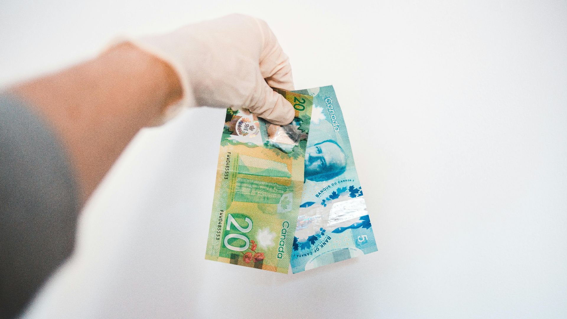 Crop anonymous male in sterile glove demonstrating different paper bills with image of President and colorful illustrations with numbers near white wall at home
