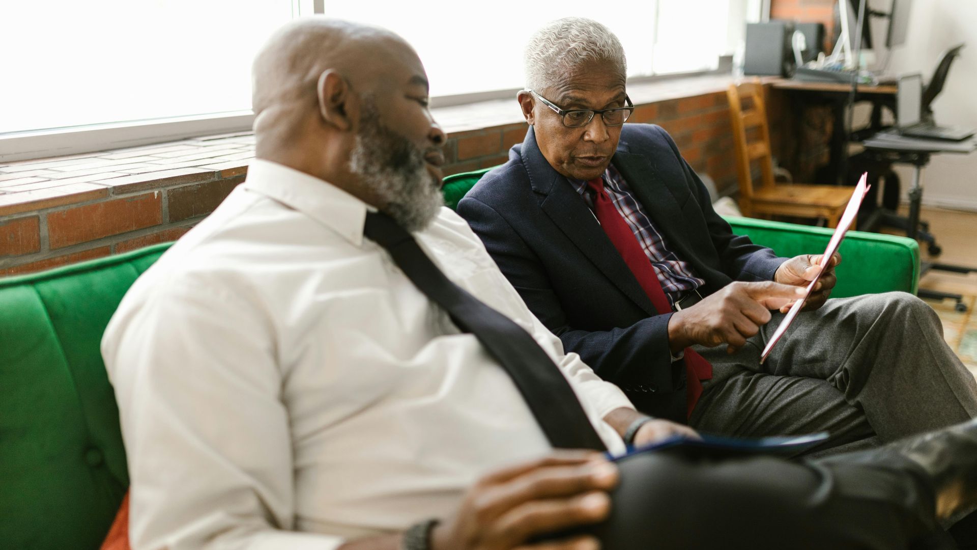 Two mature men engaged in a serious business discussion on a sofa indoors.