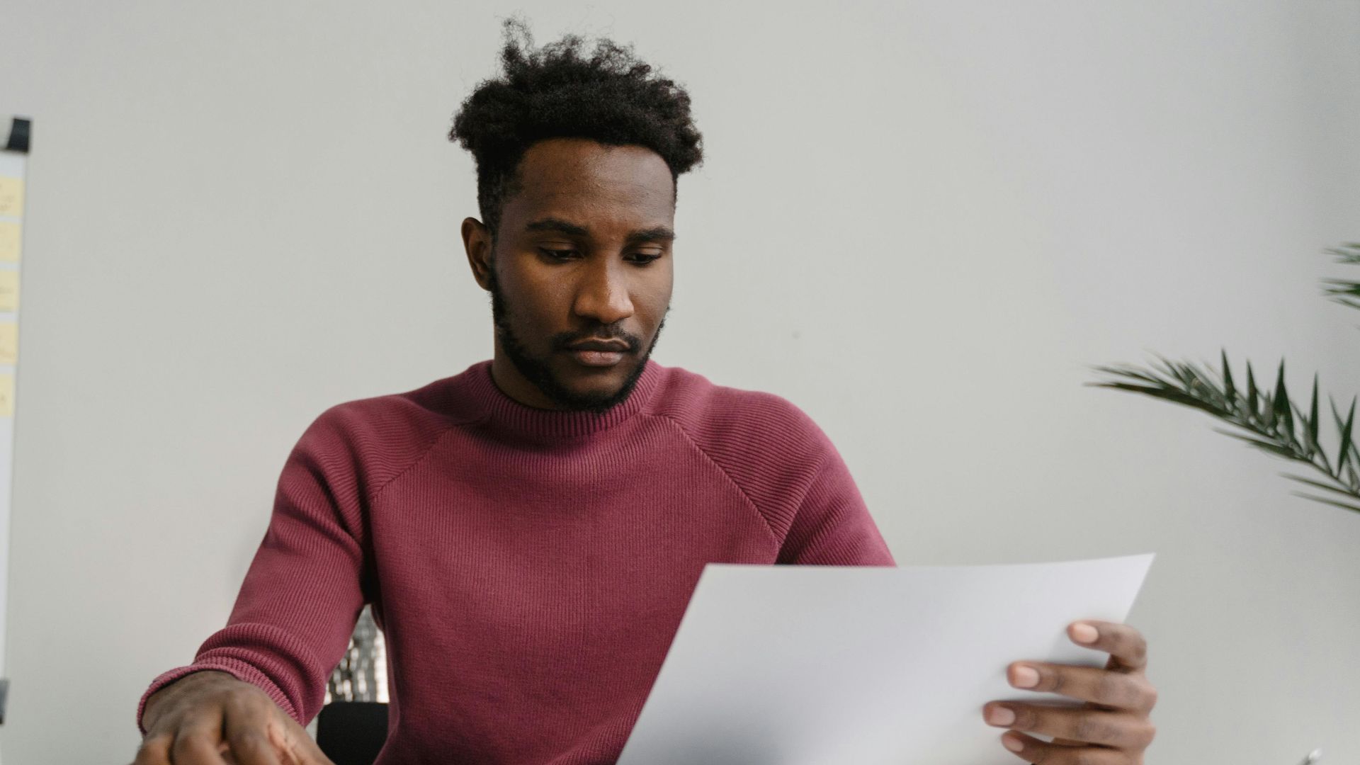 A man in a workspace analyzing a white document attentively. Modern office environment.