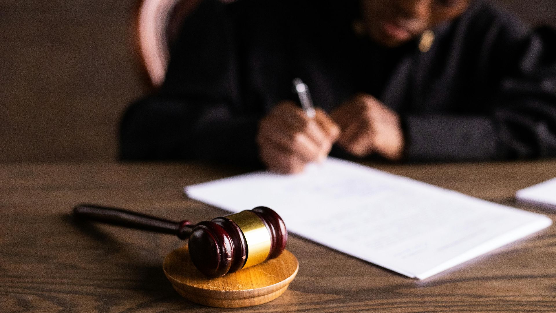 Judge signing documents at desk with focus on gavel, representing law and justice.