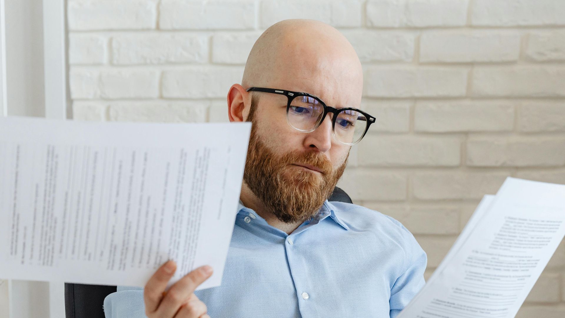 Bald bearded businessman reading financial documents in modern office setting.