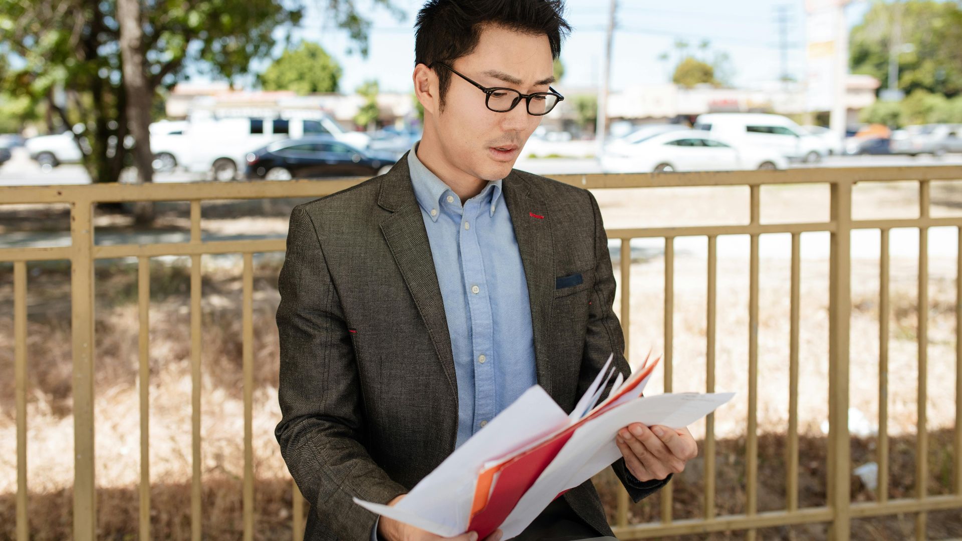 Asian businessman in a suit checking documents outdoors on a sunny day.
