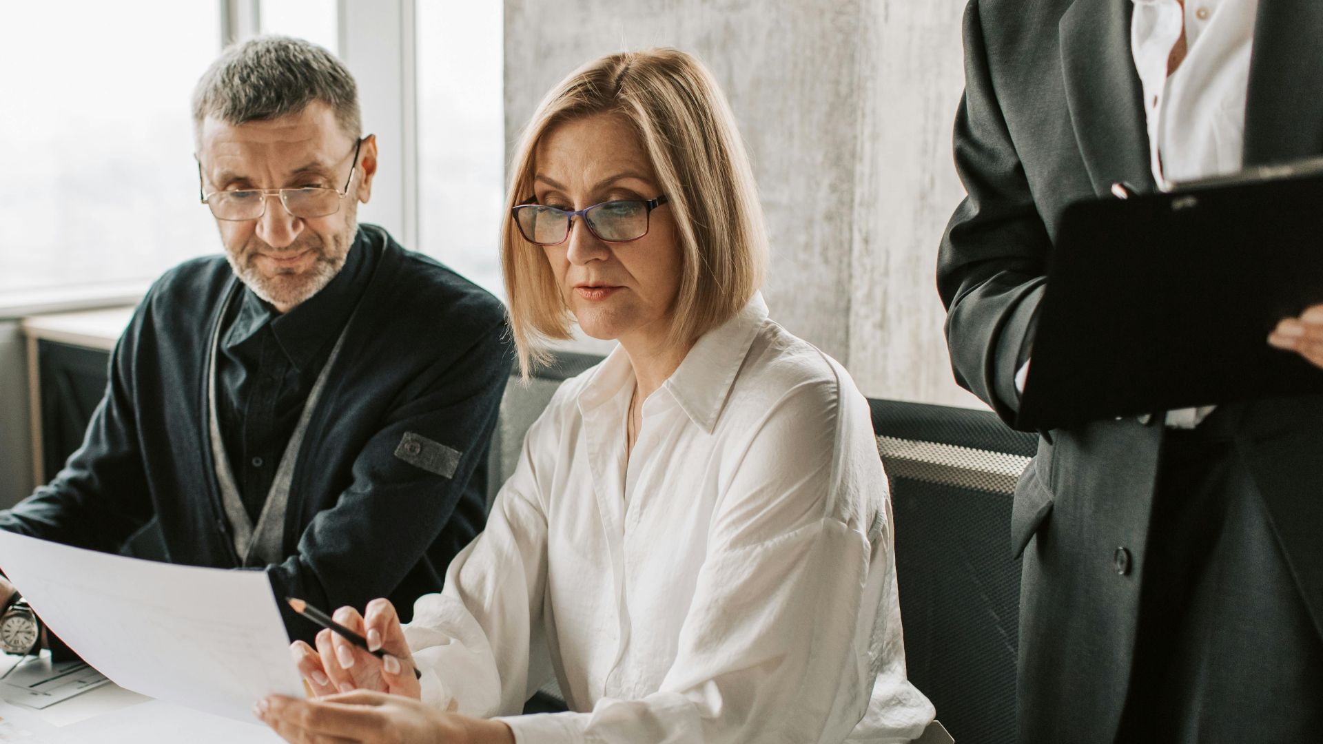 Business professionals engaged in a meeting, analyzing documents and charts in a modern office.