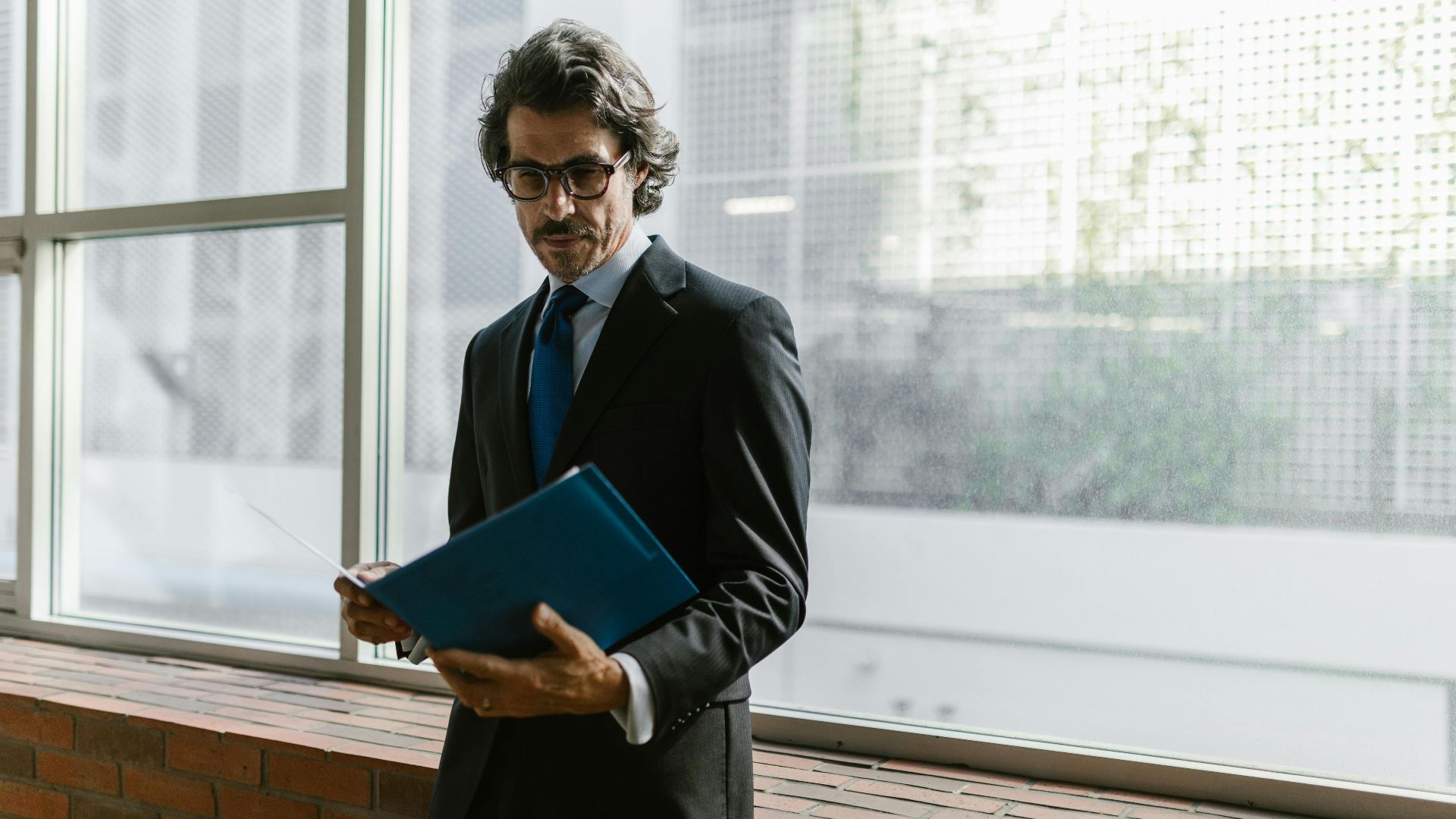 Focused businessman in suit and tie reading documents indoors with natural light.