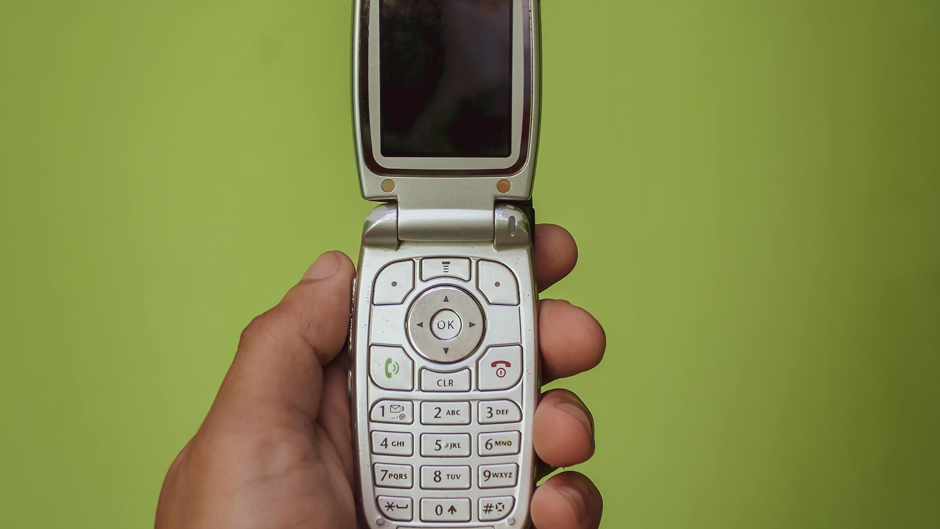 Retro Motorola flip phone held in a hand against a vibrant green background, showcasing nostalgia.