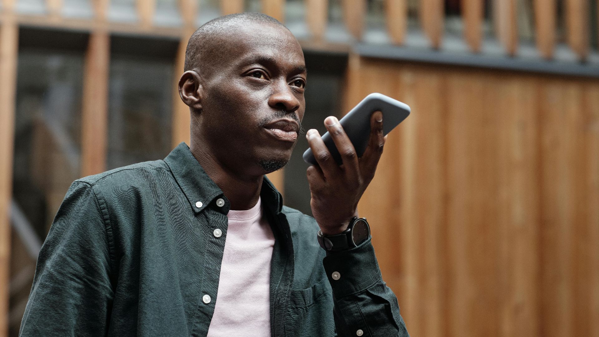 Stylish adult man using his smartphone for voice commands in an outdoor urban setting.