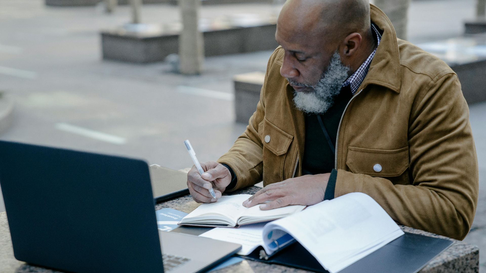 Mature man working with laptop and notebook outdoors, focusing on business tasks.