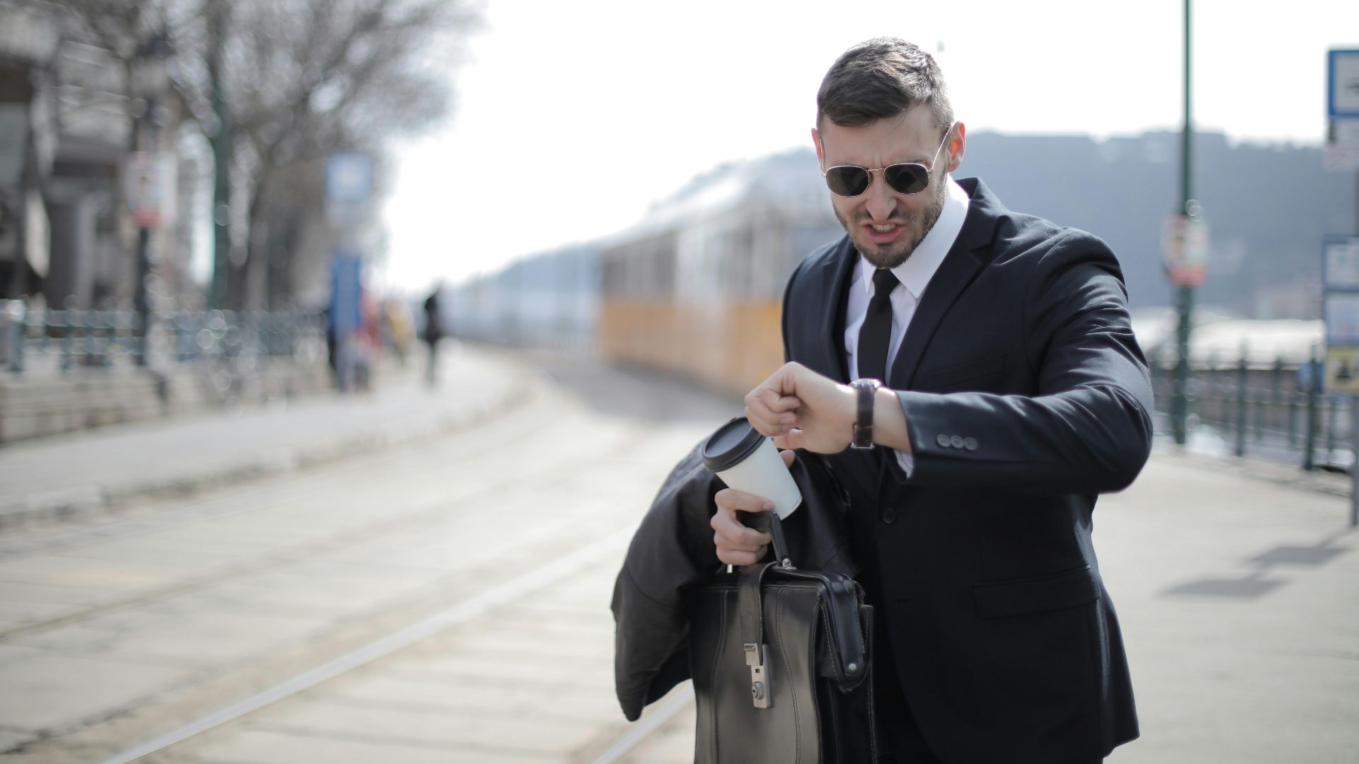 A businessman in a suit checks his watch while rushing on a sunny day in the city.