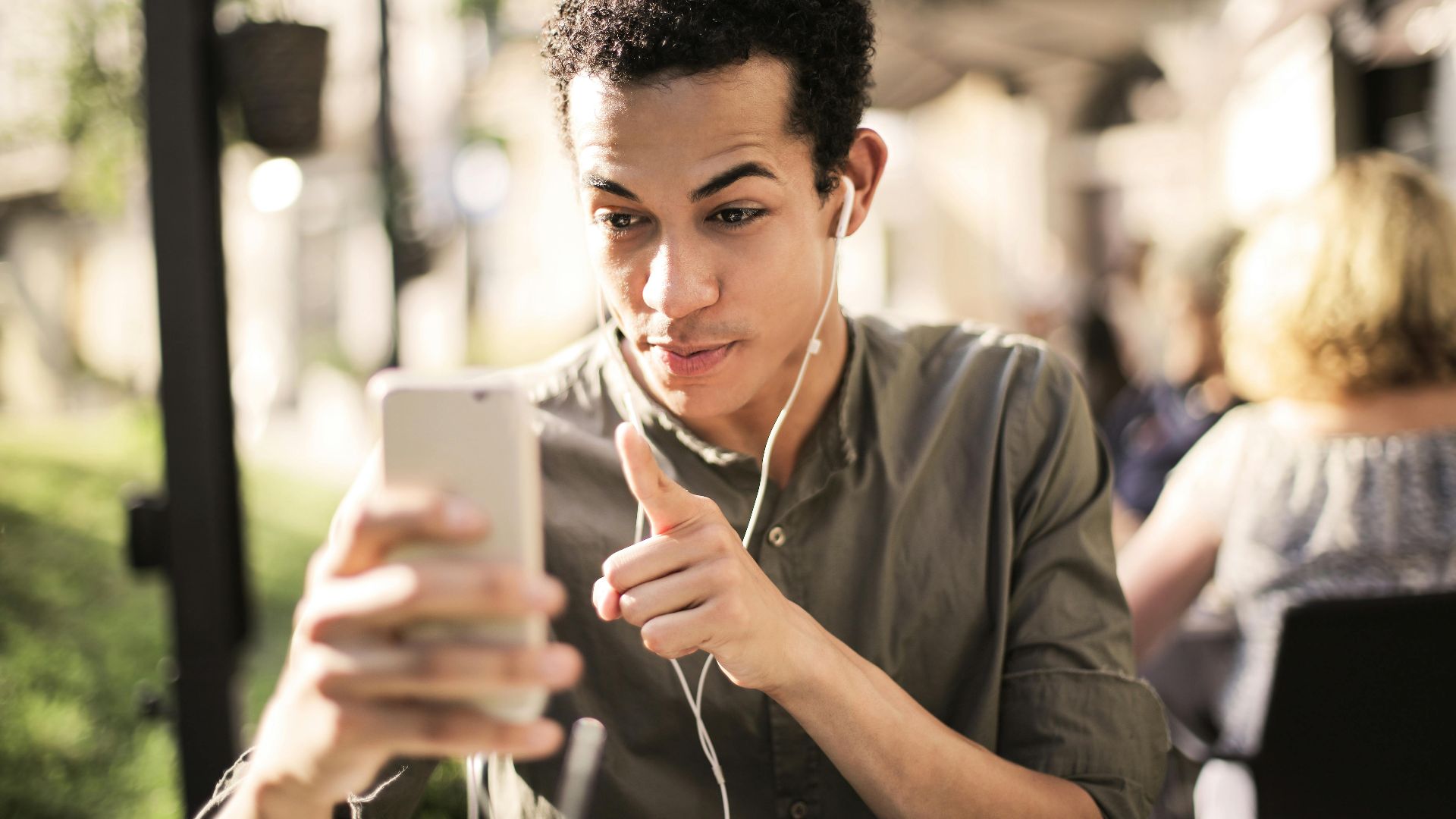 Young man wearing headphones, engaging in a video call outdoors on a sunny day.