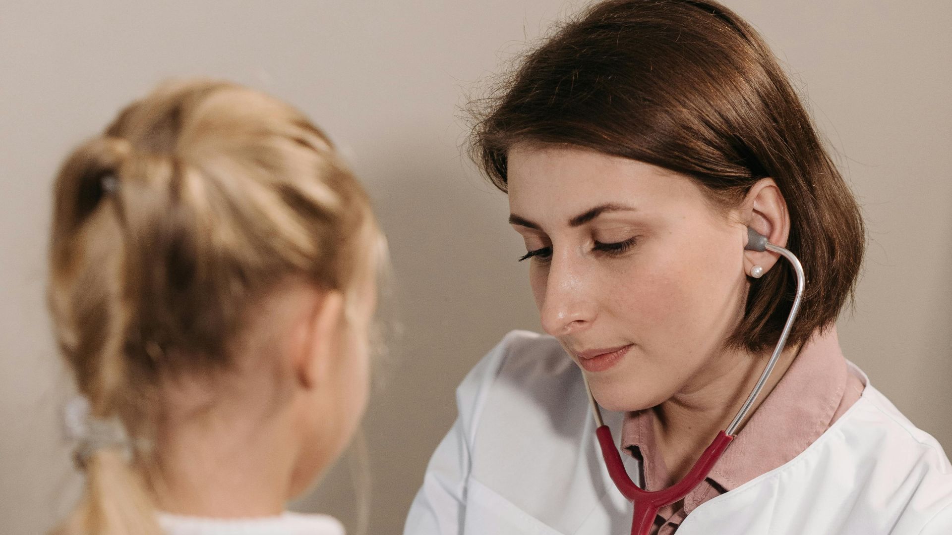 A female doctor examining a child with a stethoscope during a pediatric check-up in a clinic.