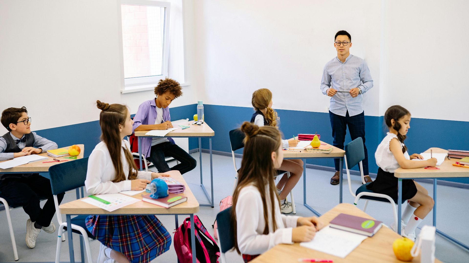 Teacher instructing a diverse group of elementary students in a modern classroom setting.
