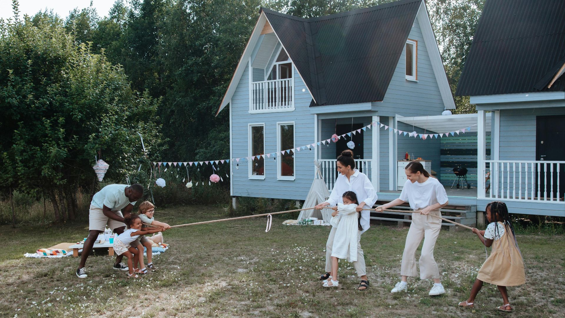 Happy family playing tug of war in front of cozy houses during a summer day.