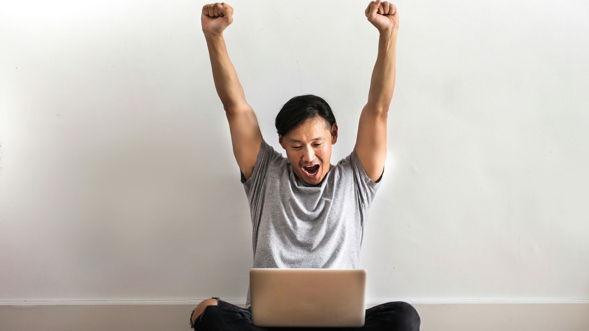 Young man joyfully celebrating success with a laptop indoors.