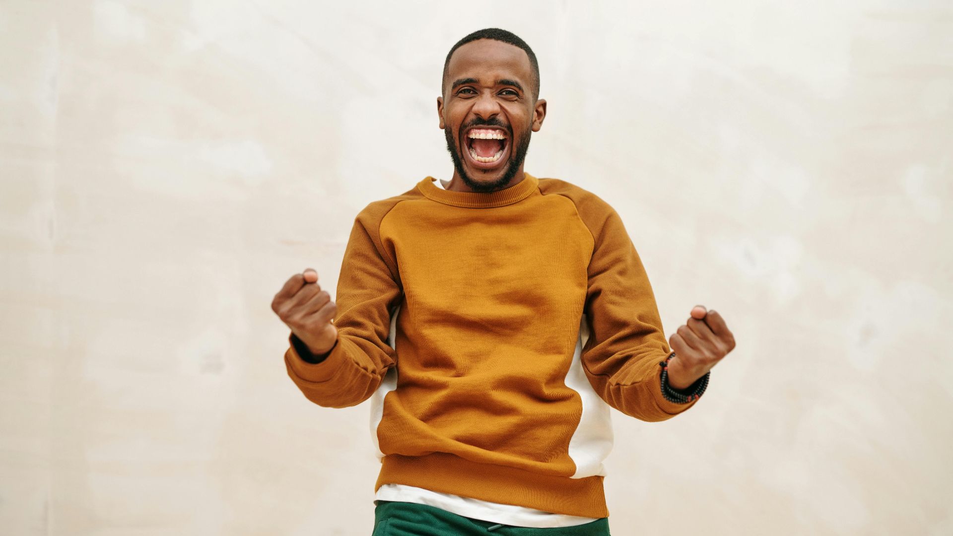 A joyful man with a beard in a sweater, expressing excitement and celebration indoors.